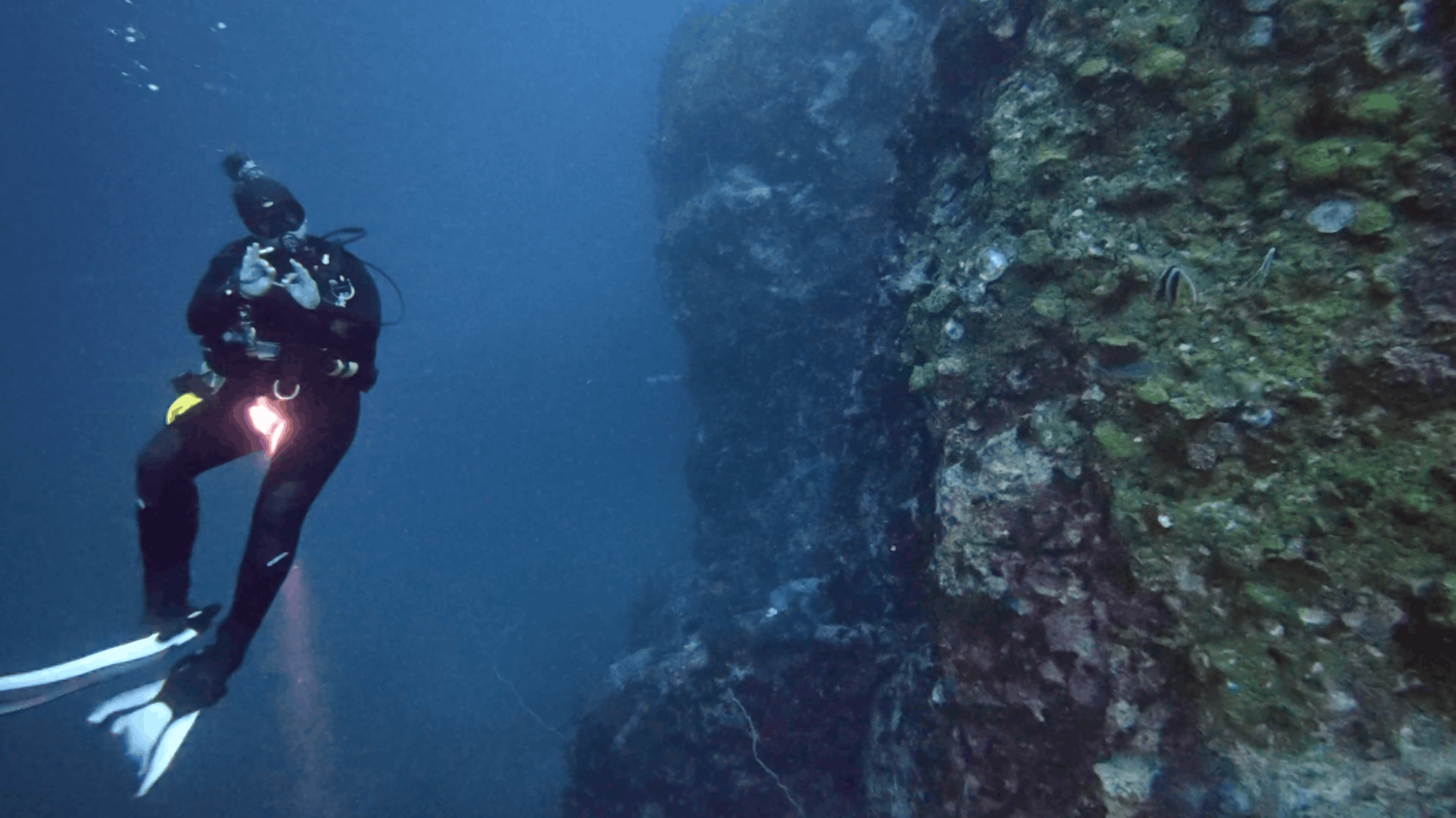 Scuba diver descending alongside the granite wall of Chumphon Pinnacle, Koh Tao