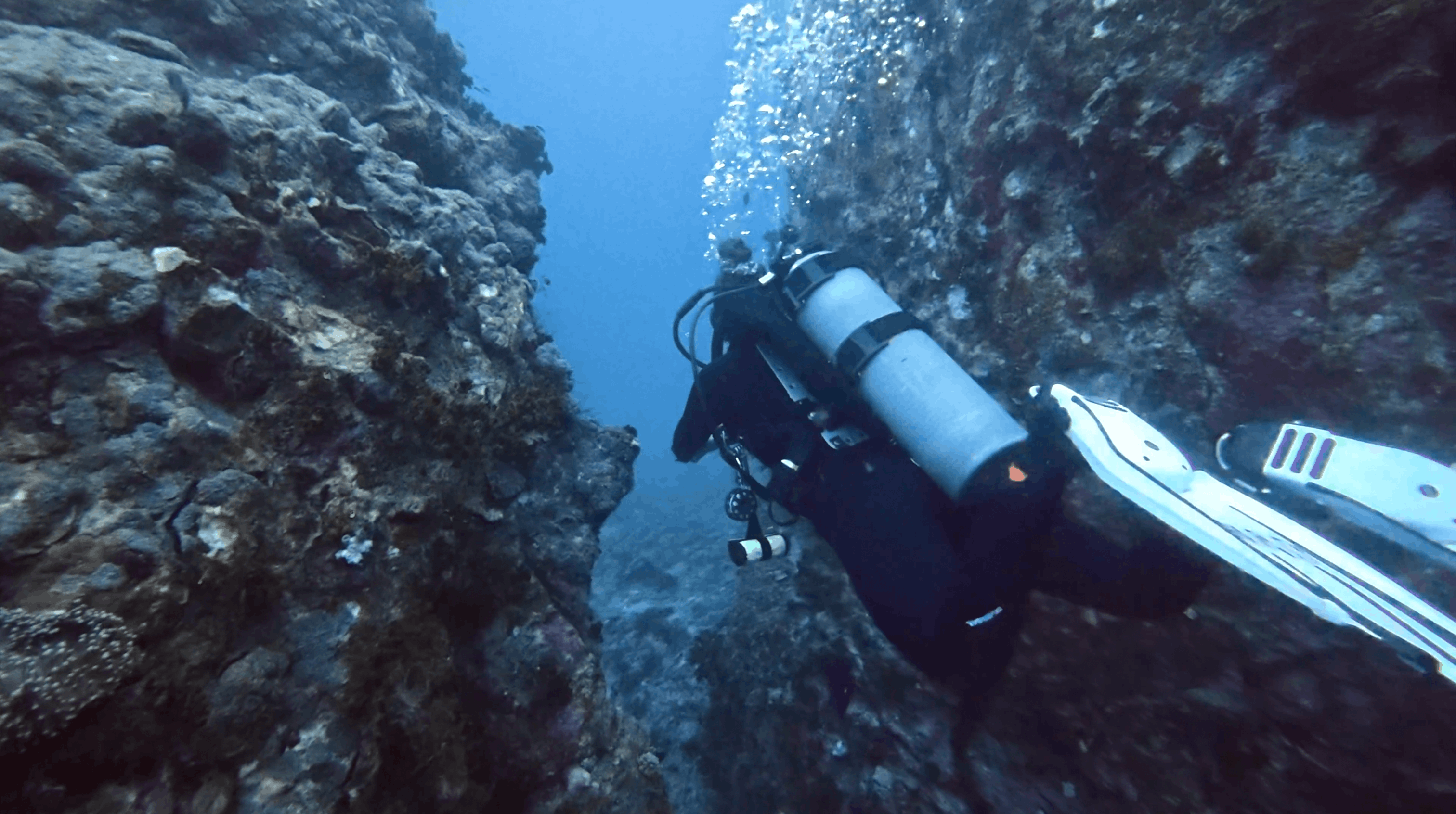 Scuba diver passing through the boulder swim through at Chumphon Pinnacle, Koh Tao