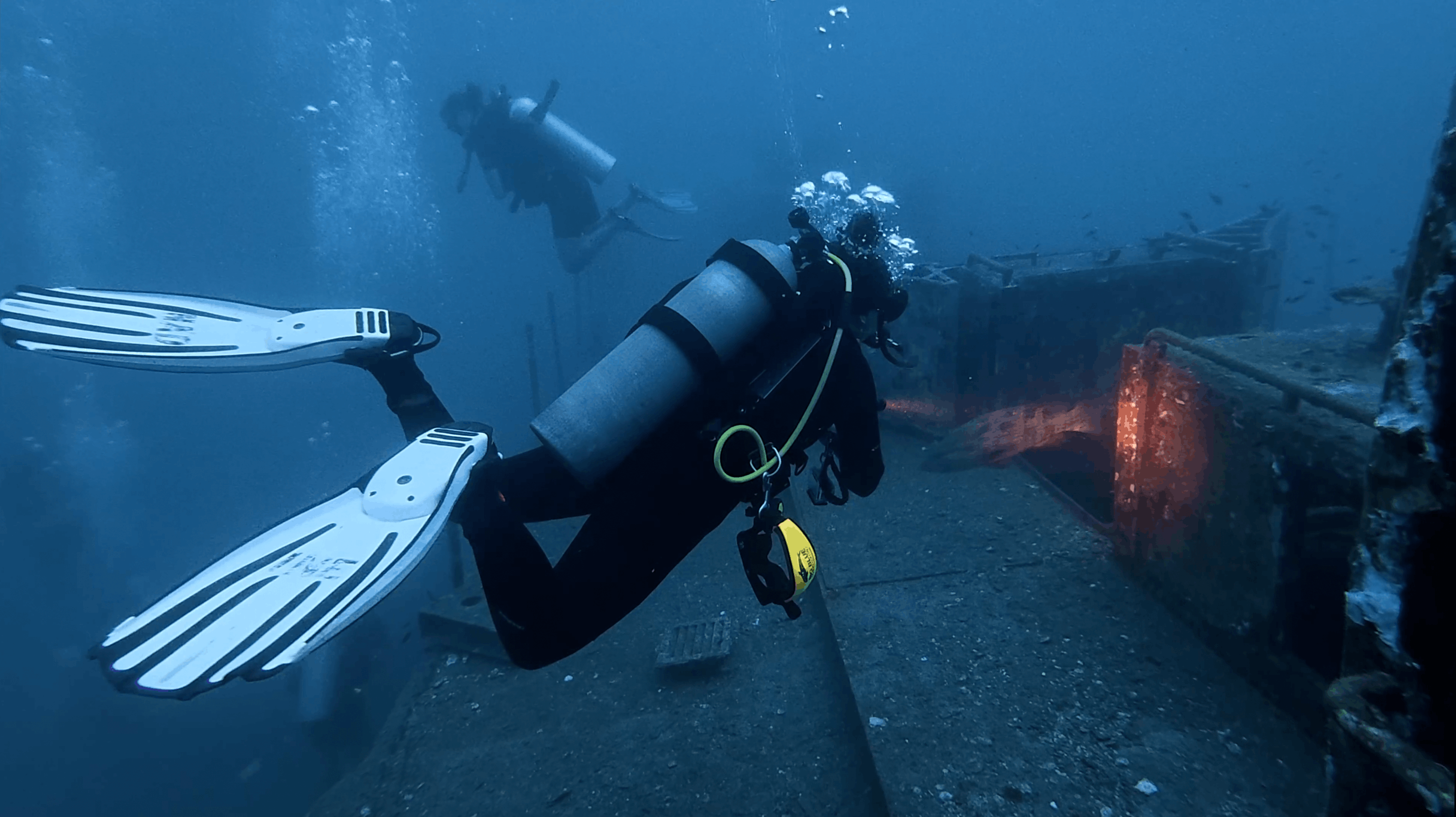Two divers finning along the deck of the HTMS Suphairin wreck, Koh Tao