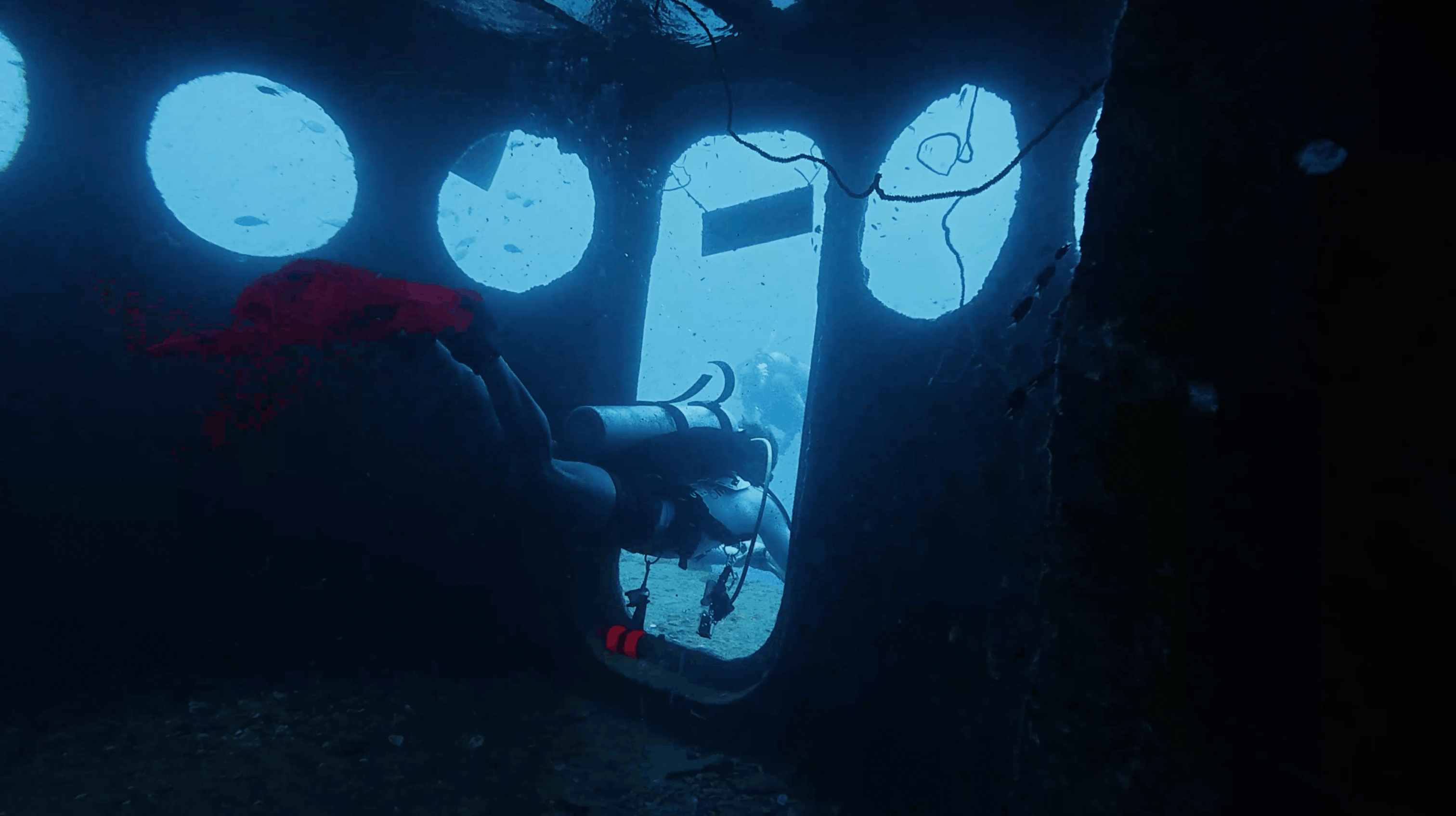 Scuba diver leaving the HTMS Sattakut through a doorway, seen from inside the hull
