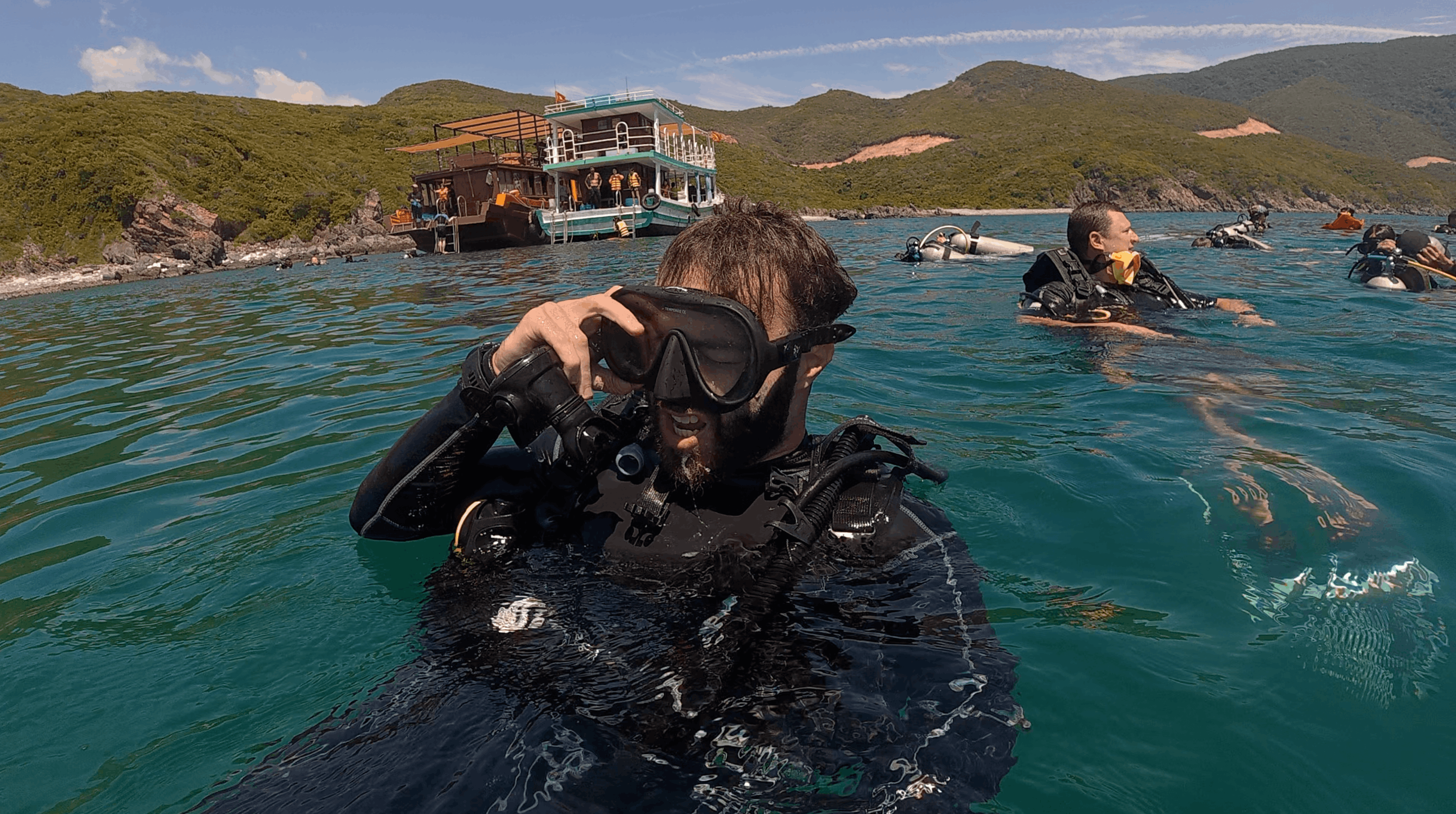 Divemaster Austin at the surface in scuba gear with the dive boat and island behind him in Nha Trang, Vietnam