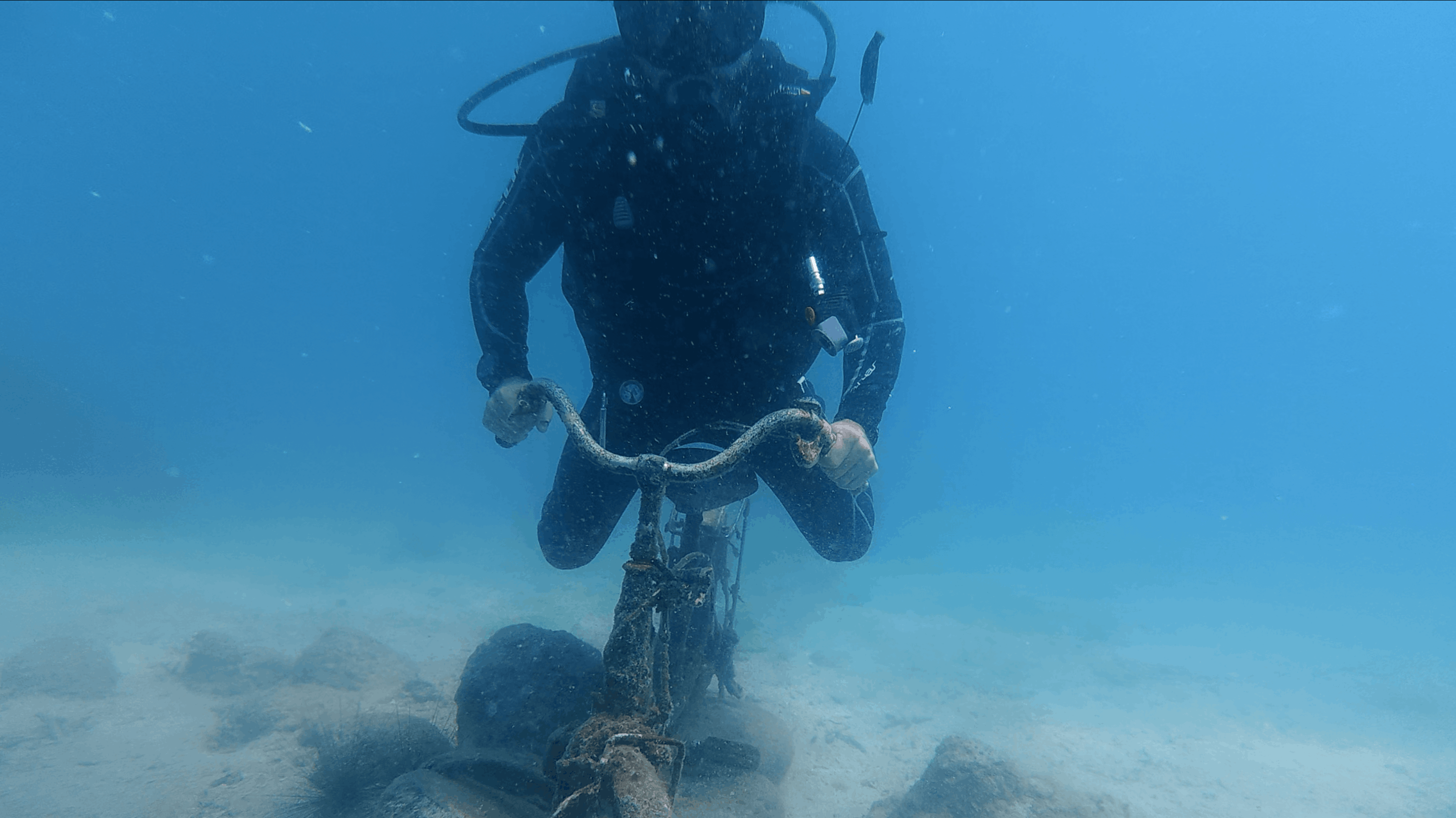 Diver holding the handlebars of a rusted bicycle standing on the sandy bottom at Dam Bay, Nha Trang, Vietnam