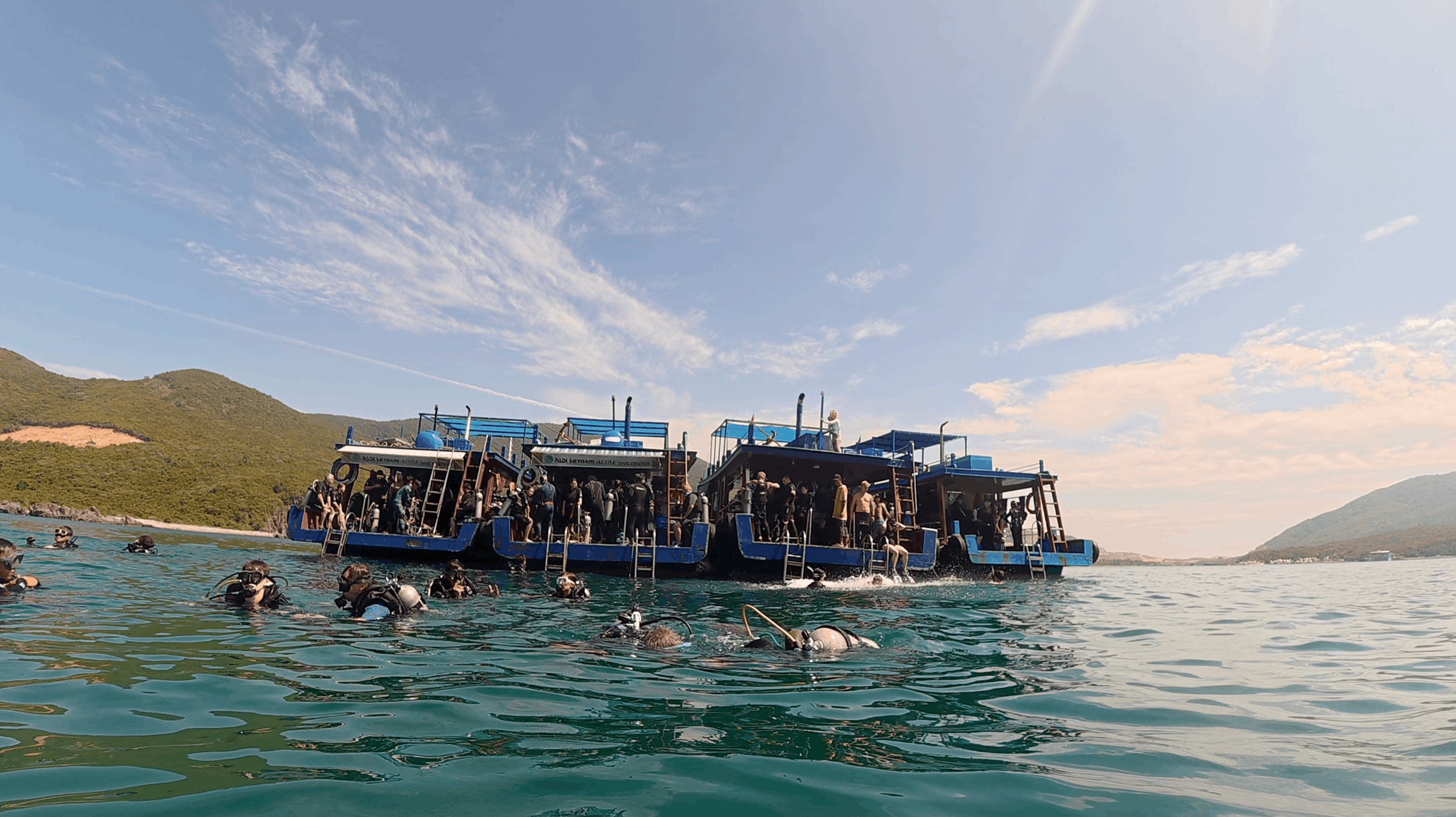 Divers in the water beside the blue dive boat with the island behind at Dam Bay, Nha Trang, Vietnam
