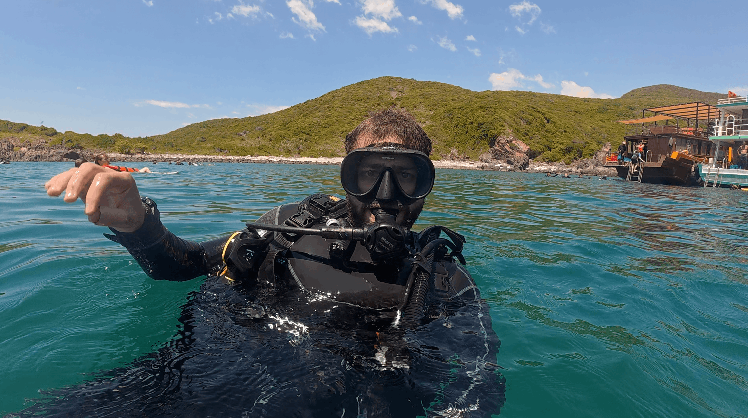 Austin at the surface in mask and regulator with the dive boat and island behind at Dam Bay, Nha Trang, Vietnam