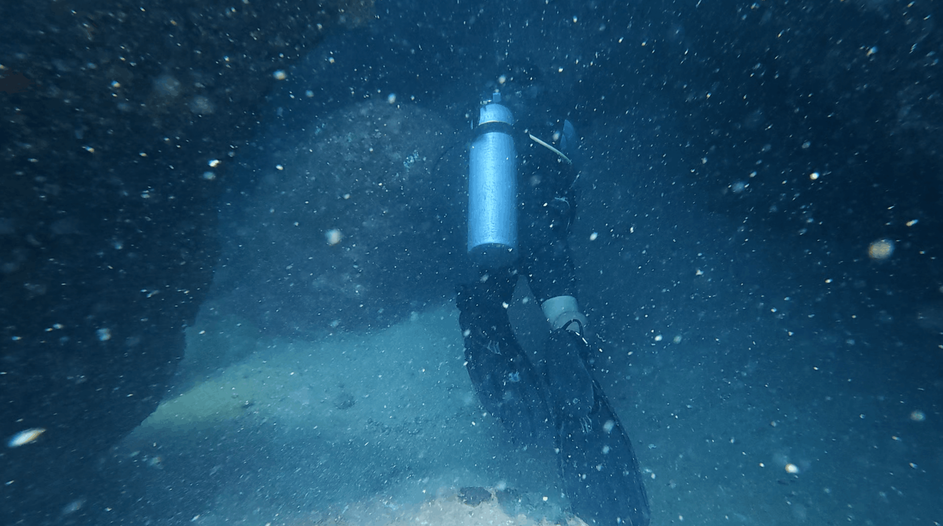 Diver with a blue tank moving through a dark narrow passage in the rock at Madonna Rock, Nha Trang, Vietnam