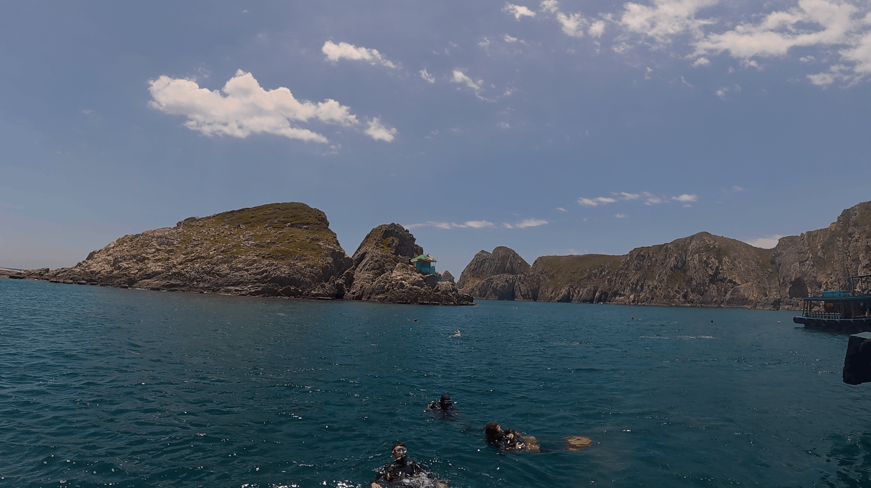 Rocky islets above the dive site with divers at the surface and a dive boat moored alongside at Madonna Rock, Nha Trang, Vietnam