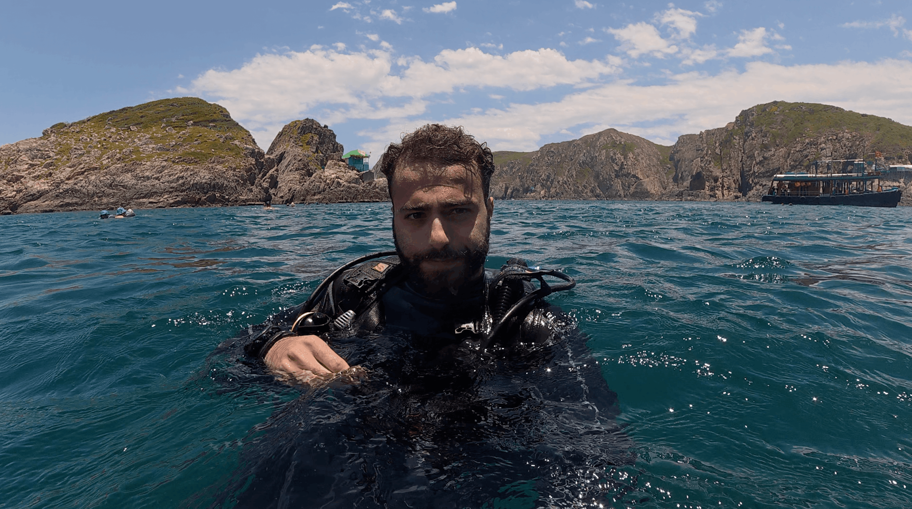 Austin at the surface in scuba gear with the rock formations and dive boat behind him at Madonna Rock, Nha Trang, Vietnam