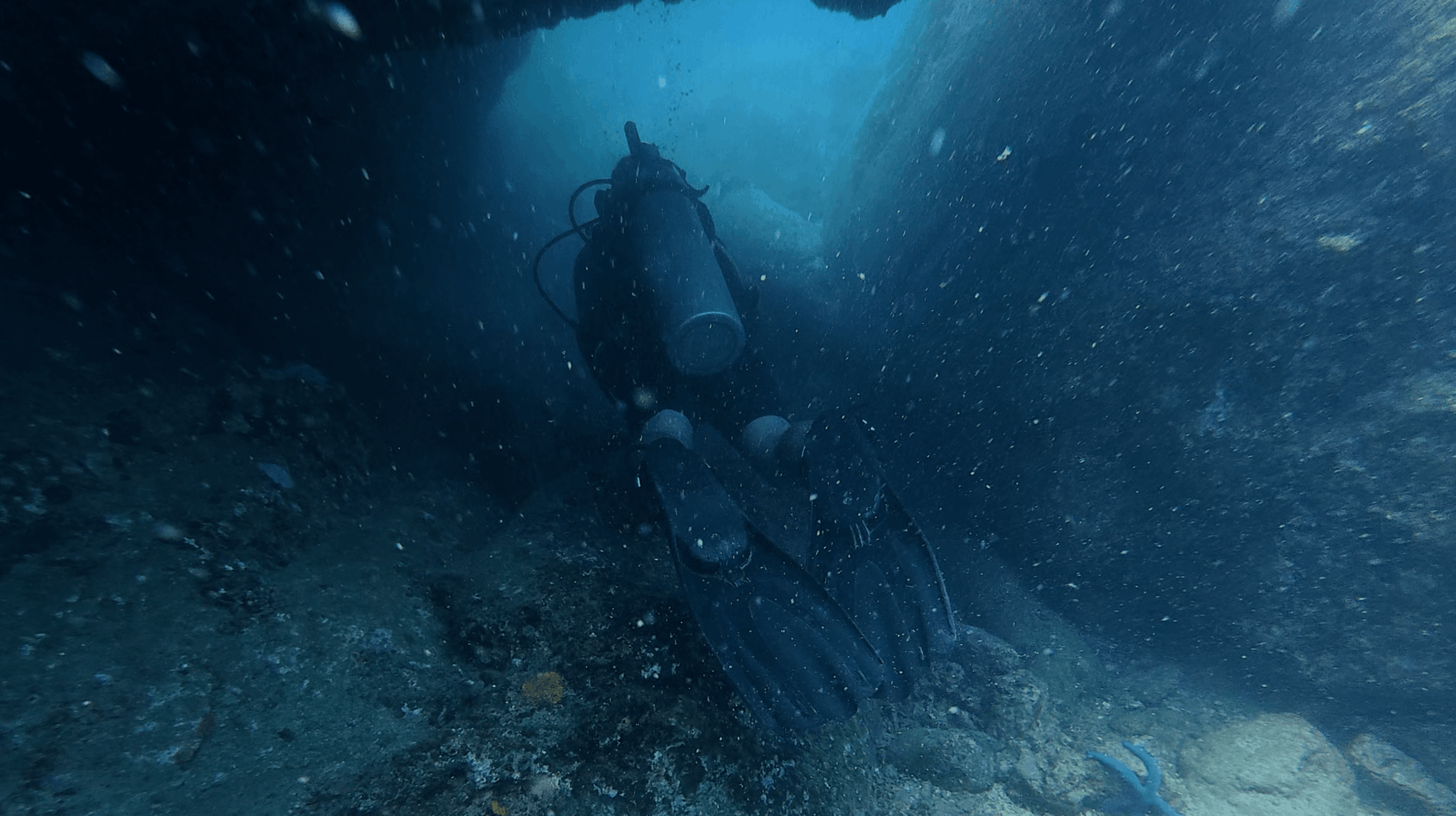Diver silhouetted swimming through a narrow gap between rock walls at Madonna Rock, Nha Trang, Vietnam
