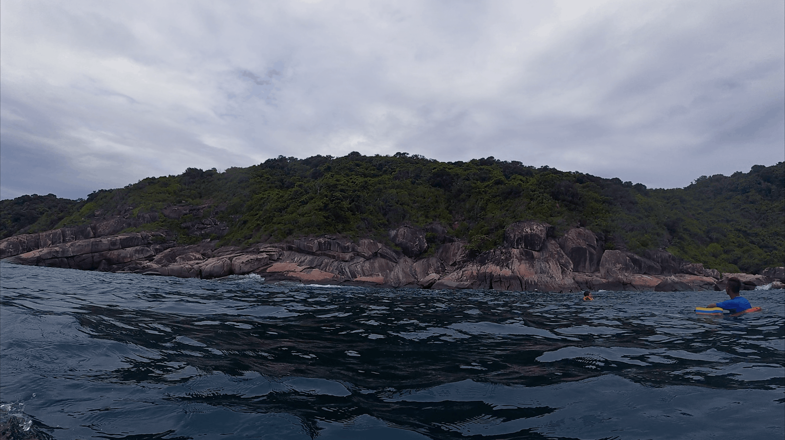 Rocky shoreline of the island seen from the water with snorkellers alongside at Hon Dai, Cham Islands, Vietnam