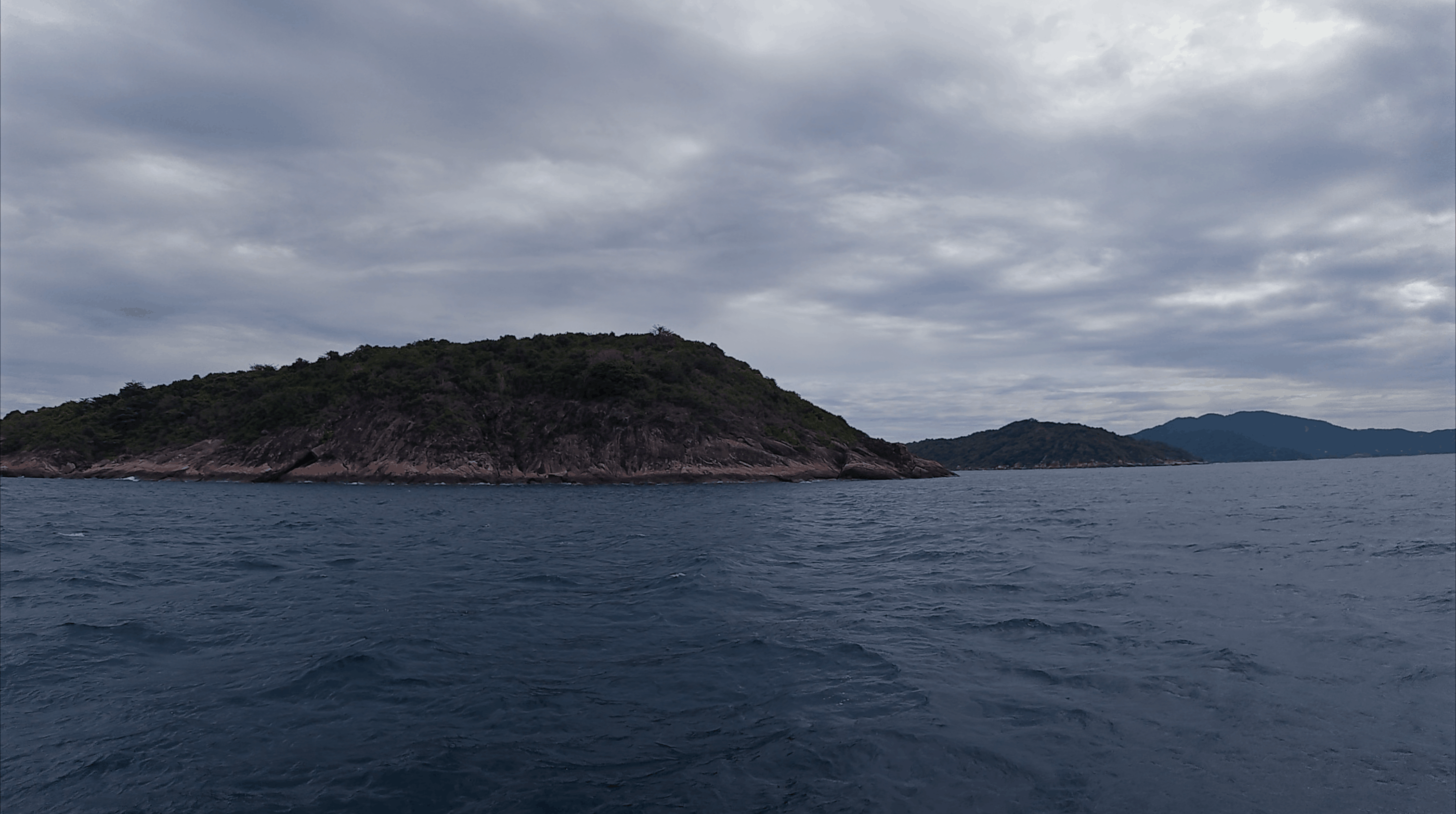 Green topped rocky island seen from the dive boat under overcast sky at Hon Dai, Cham Islands, Vietnam