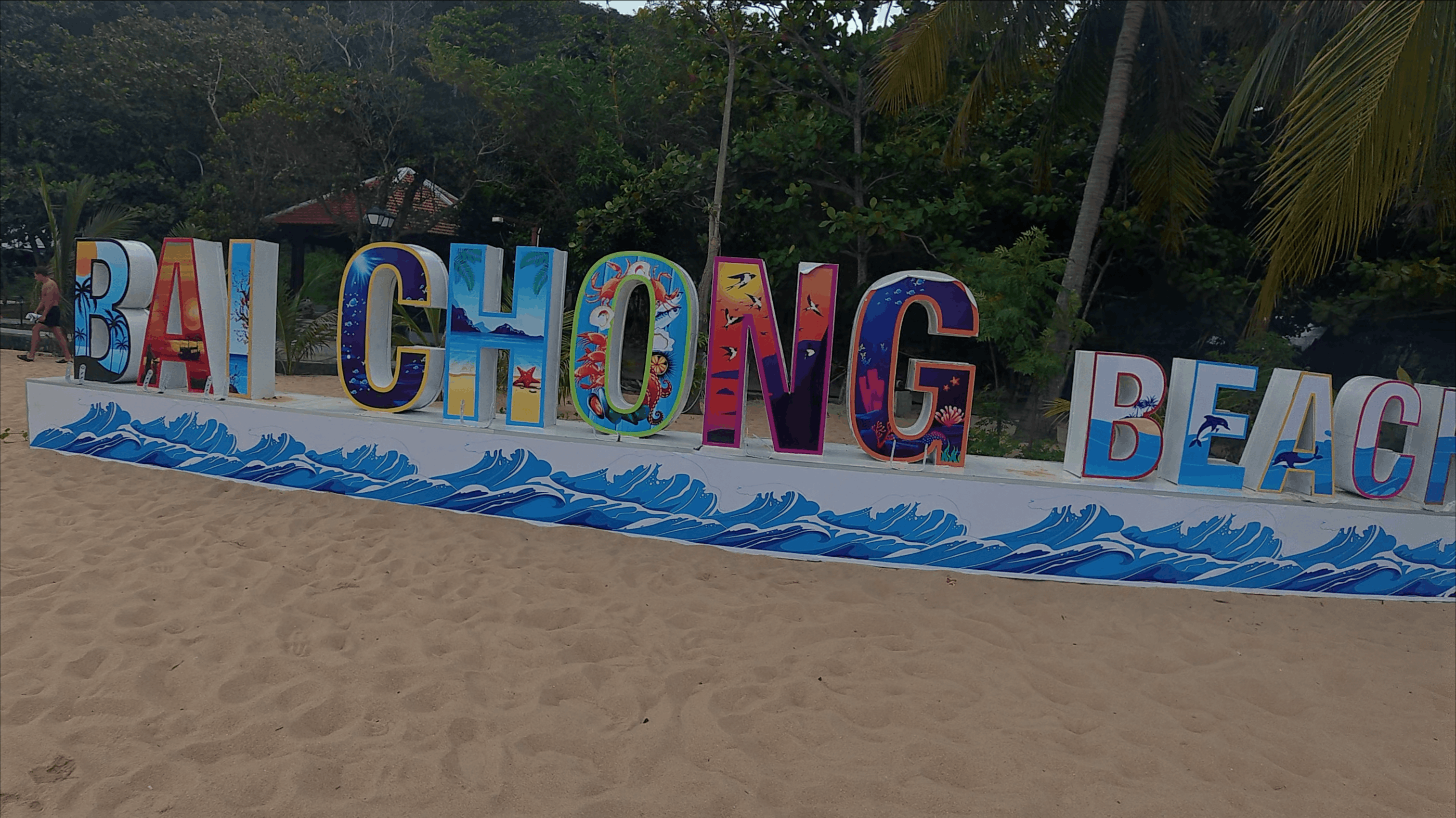 Painted Bai Chong Beach sign standing on the sand in front of palm trees at Hon Dai, Cham Islands, Vietnam