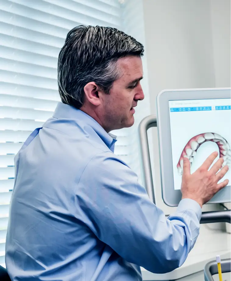 Man in blue shirt examining a digital dental model on a computer screen.