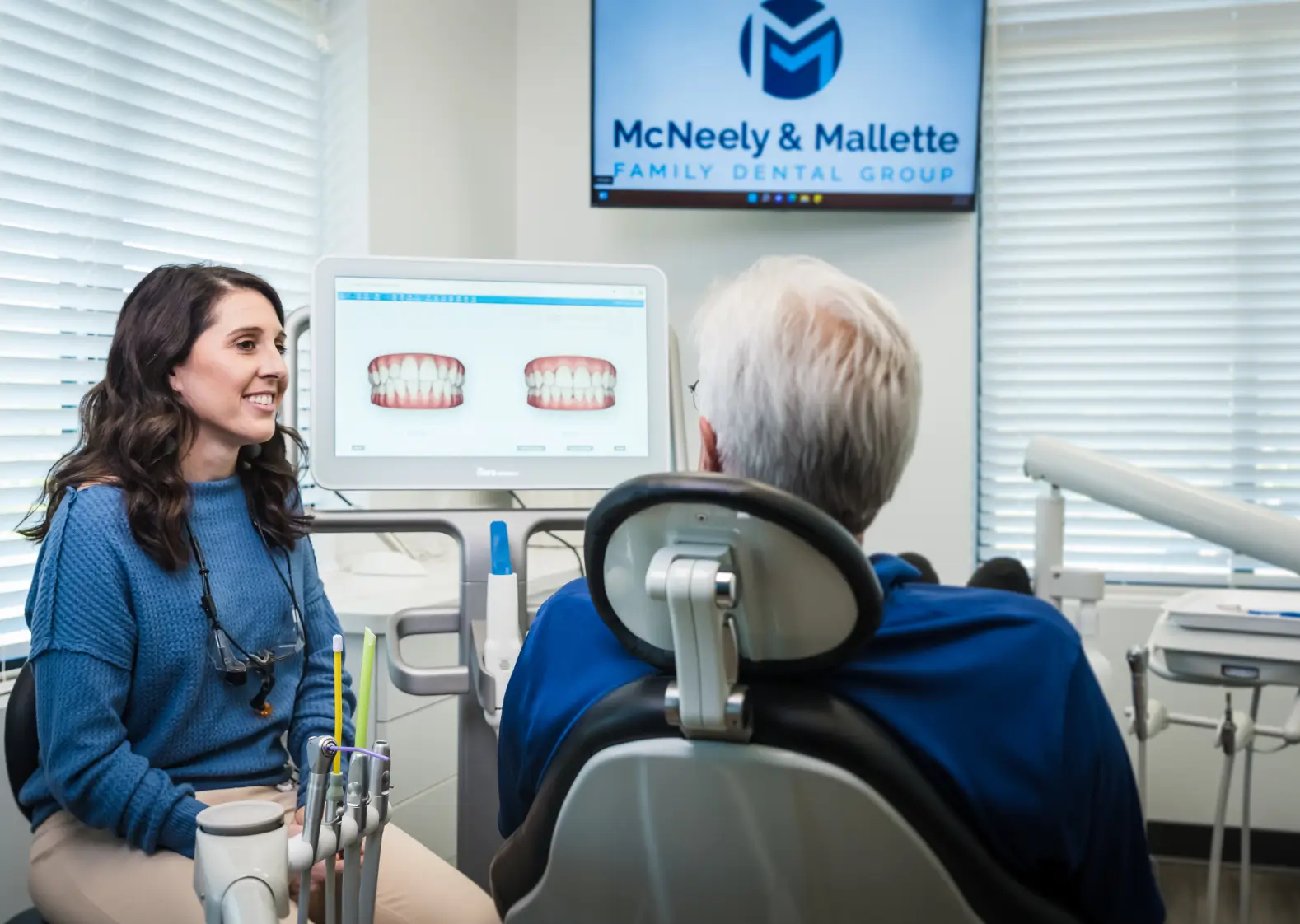 Dentist explaining 3D tooth models on a screen to a patient in a dental office.