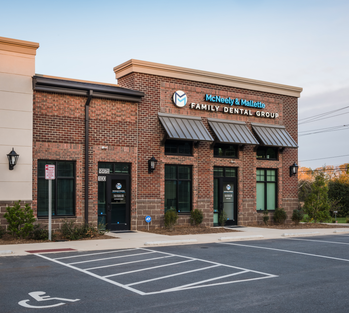 Brick building with signs for McNeely & Mallette Family Dental Group and empty handicapped parking spaces in front.