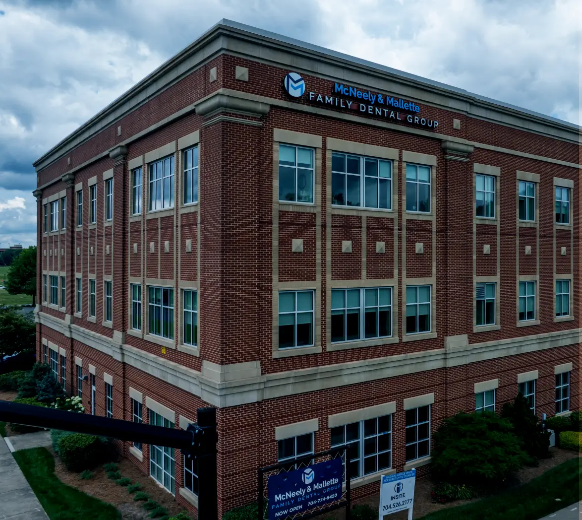 Three-story brick building with McNeely & Mallette Family Dental Group signage under a cloudy sky.