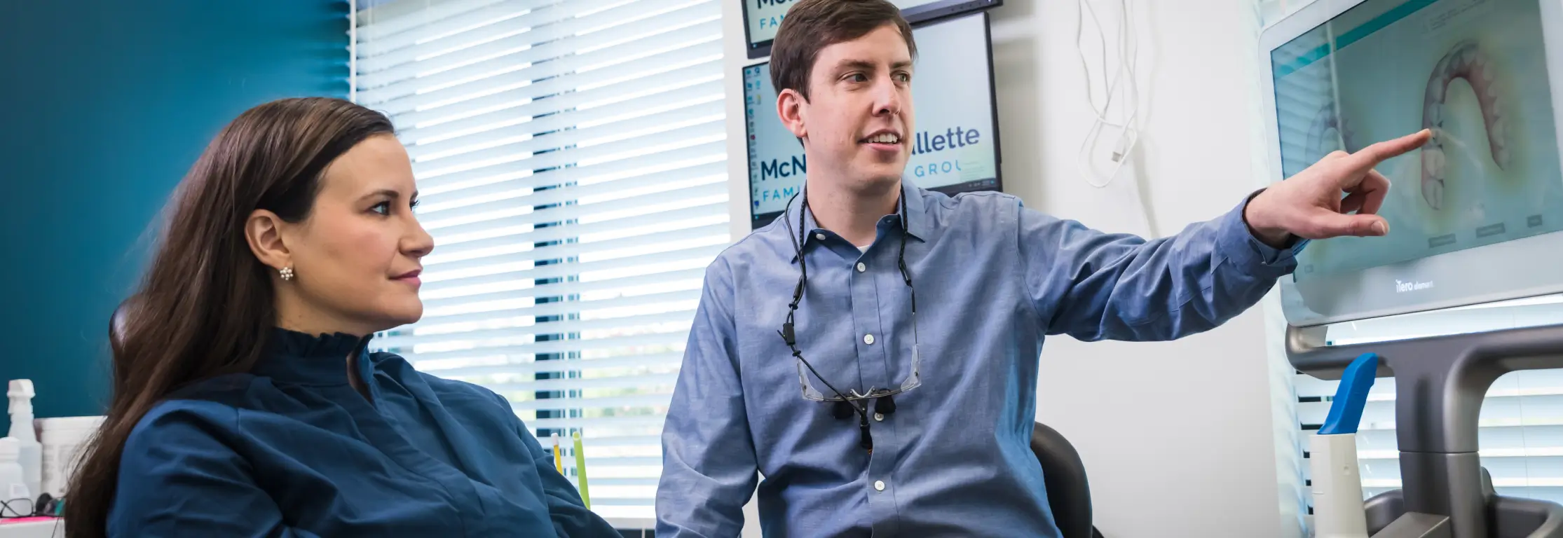 Dentist explaining a dental scan on a screen to a female patient.