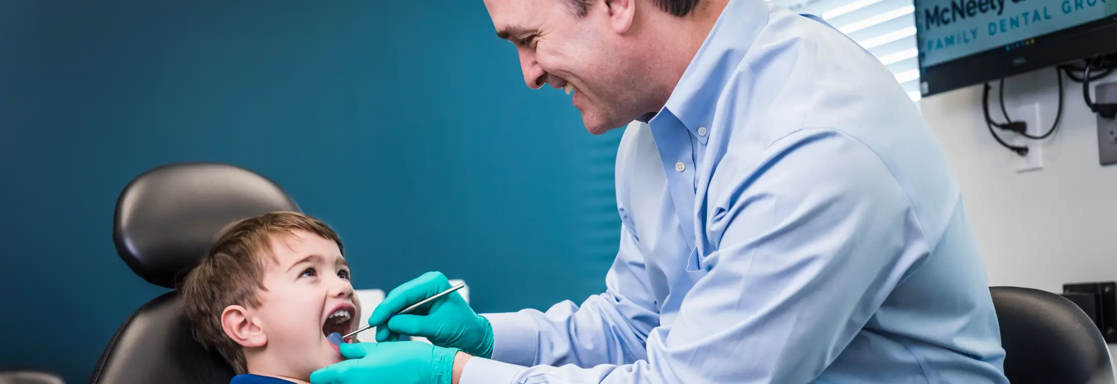 Dentist wearing gloves examining a young boy’s teeth in a dental office.