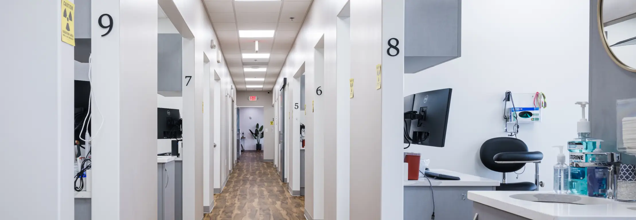 Bright medical or dental clinic hallway with numbered rooms and equipment visible in room 8.