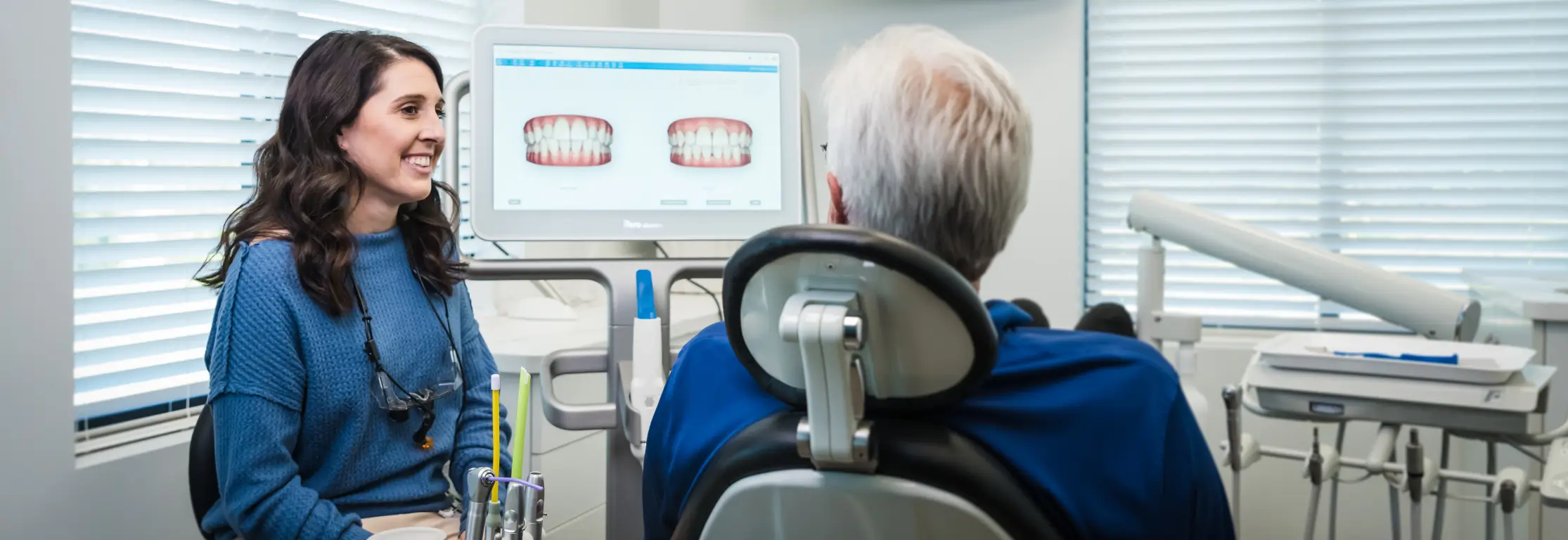 Dentist discussing dental images with an older patient seated in a dental chair.