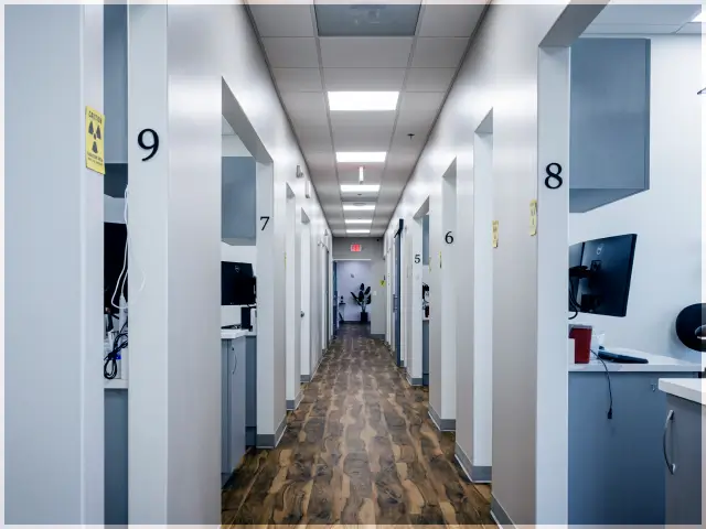 Long hallway in a modern clinic or office with numbered rooms and wood-patterned flooring.
