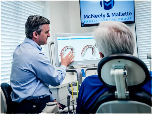 Dentist explaining dental images on a monitor to an elderly patient in a dental office of McNeely & Mallette Family Dental Group.