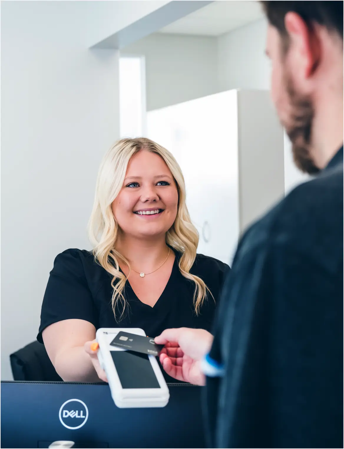 Smiling woman holding a card reader as a man pays with a credit card.