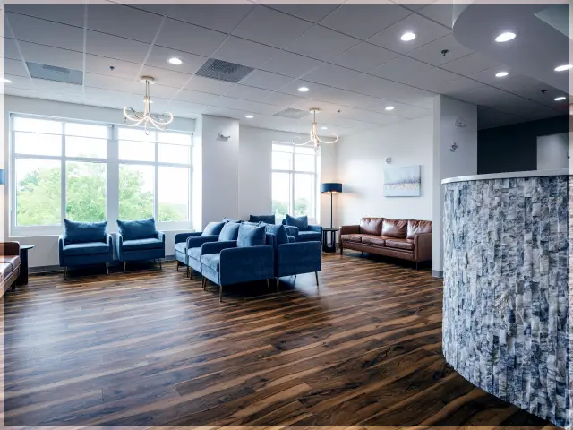 Modern waiting room with blue and brown sofas, large windows, wooden flooring, and contemporary lighting fixtures.