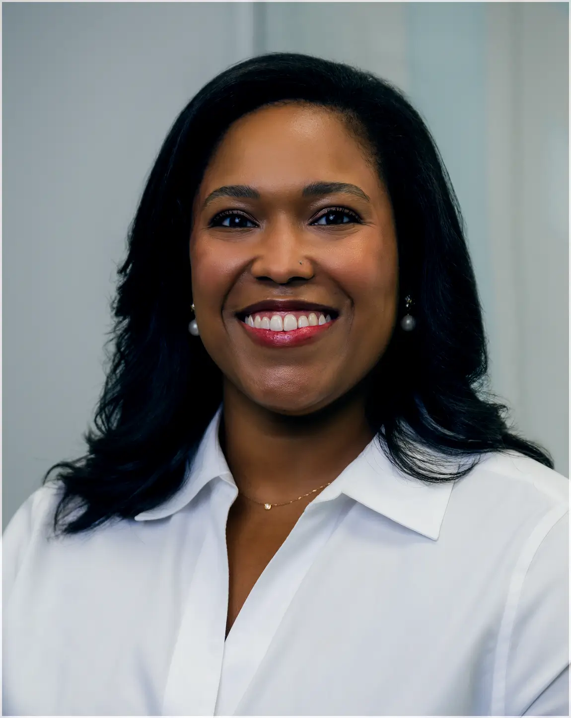 Smiling woman with dark hair wearing pearl earrings and a white collared shirt.
