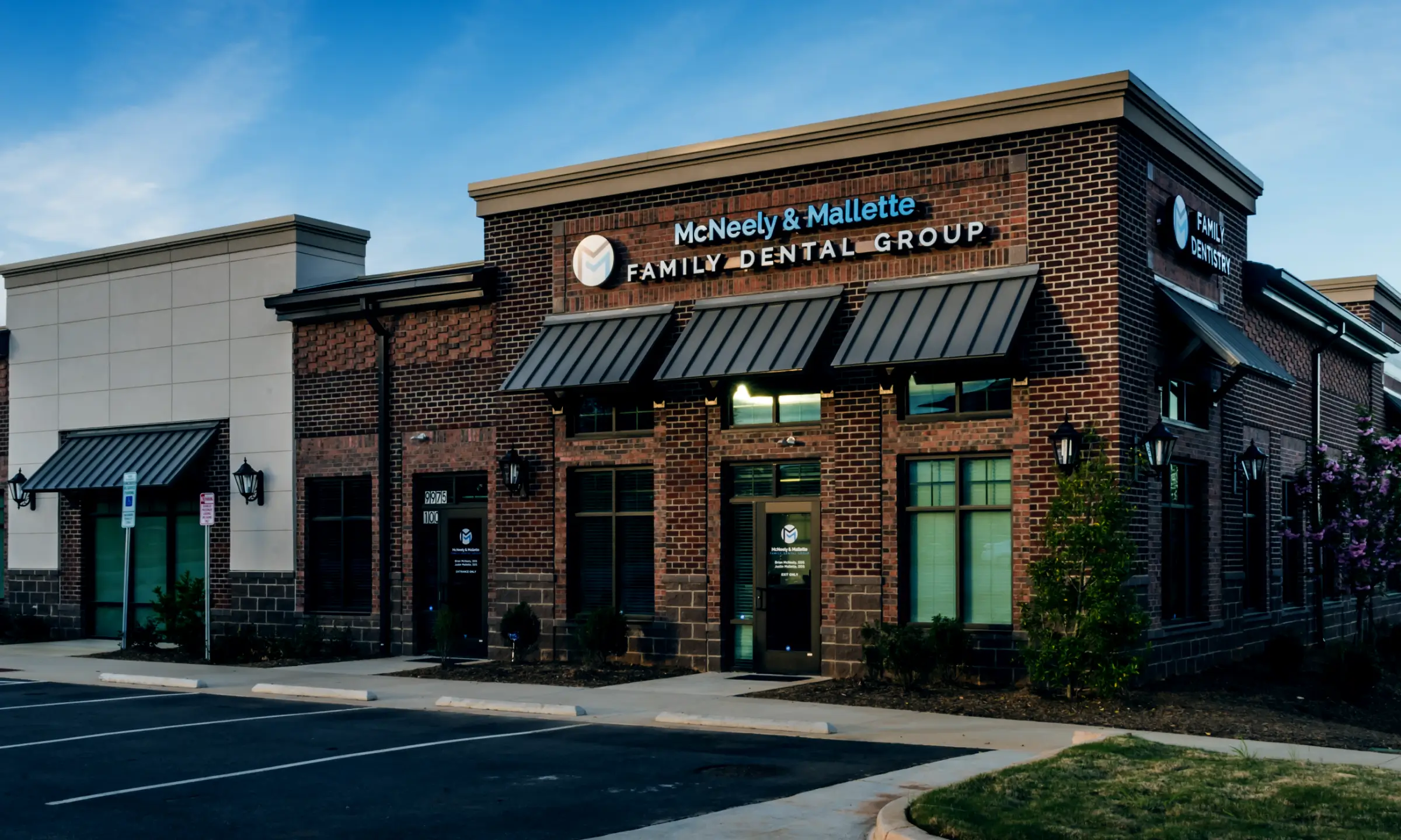 Exterior view of McNeely & Mallette Family Dental Group brick building with awnings and parking spaces in front.