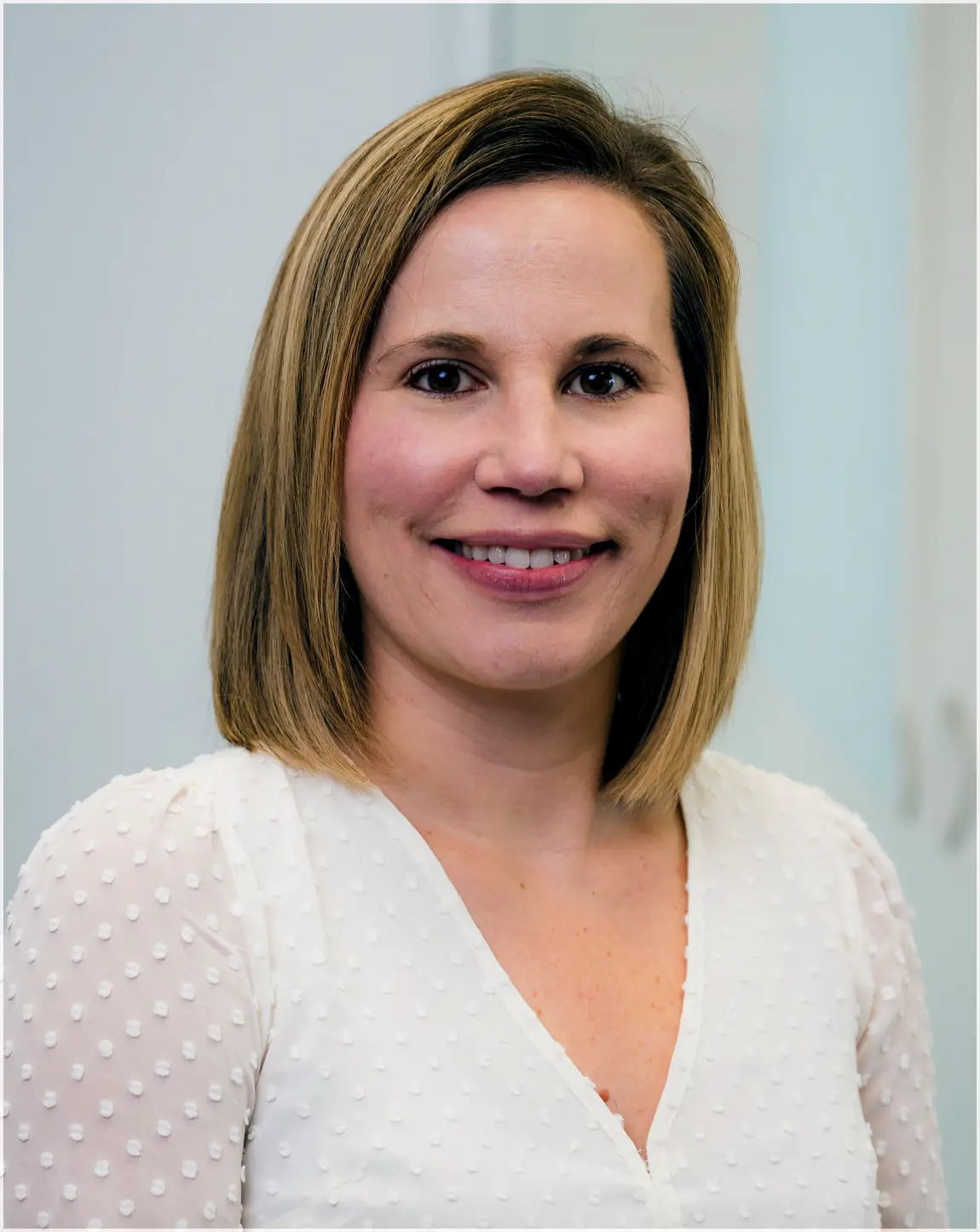 Smiling woman with shoulder-length blonde hair wearing a white textured blouse.