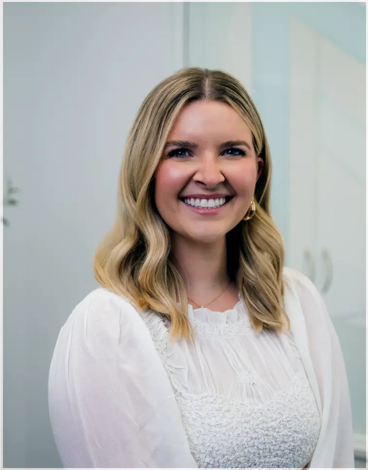 Smiling woman with shoulder-length blonde hair wearing a white blouse.