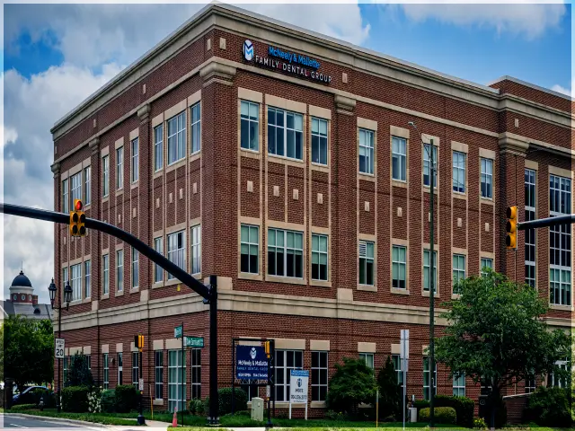 Three-story brick building housing McNeely & Mallette Family Dental Group at a street corner with traffic lights and street signs.