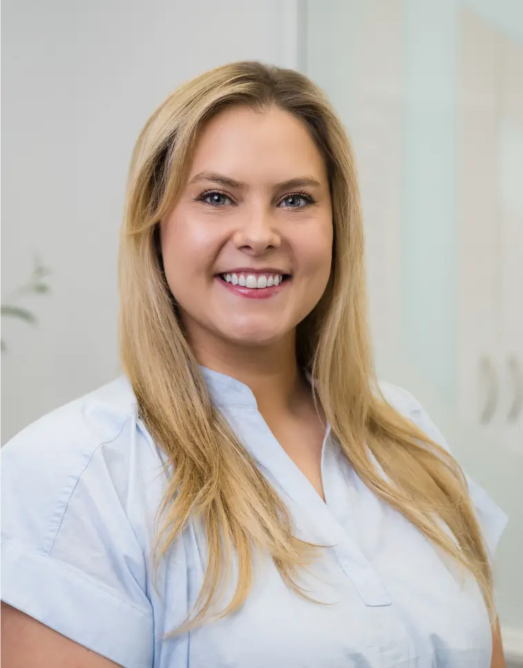 Smiling woman with long blonde hair wearing a light blue shirt in a bright indoor setting.