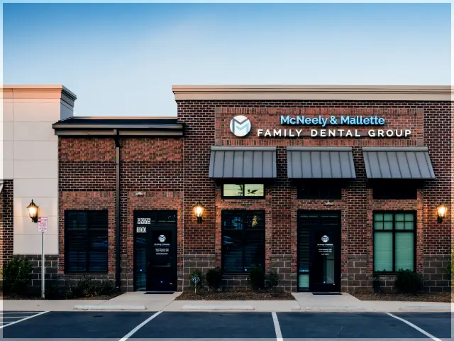 Brick building with signs for McNeely & Mallette Family Dental Group under a clear blue sky.