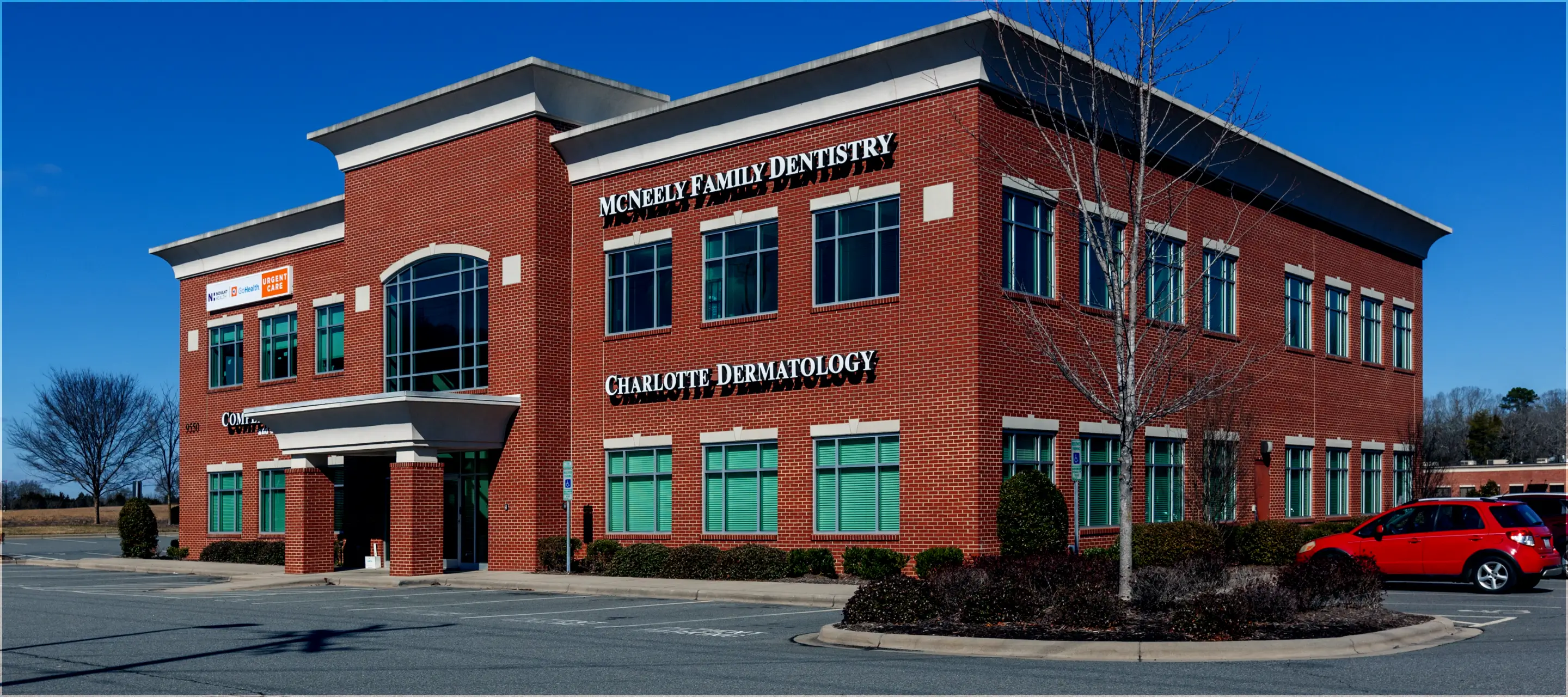 Red brick two-story medical office building with signs for McNeely Family Dentistry, Charlotte Dermatology, and Novant Health Urgent Care on a clear day.