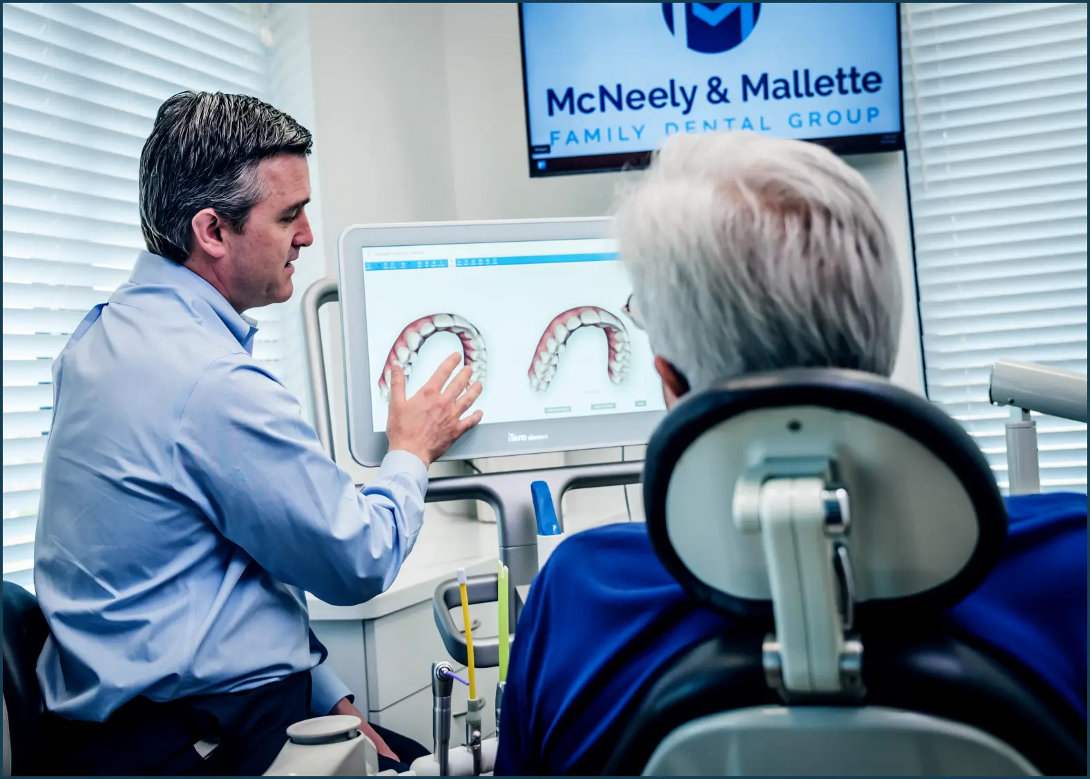 Dentist explaining dental scan images on a screen to a seated patient in a dental office.