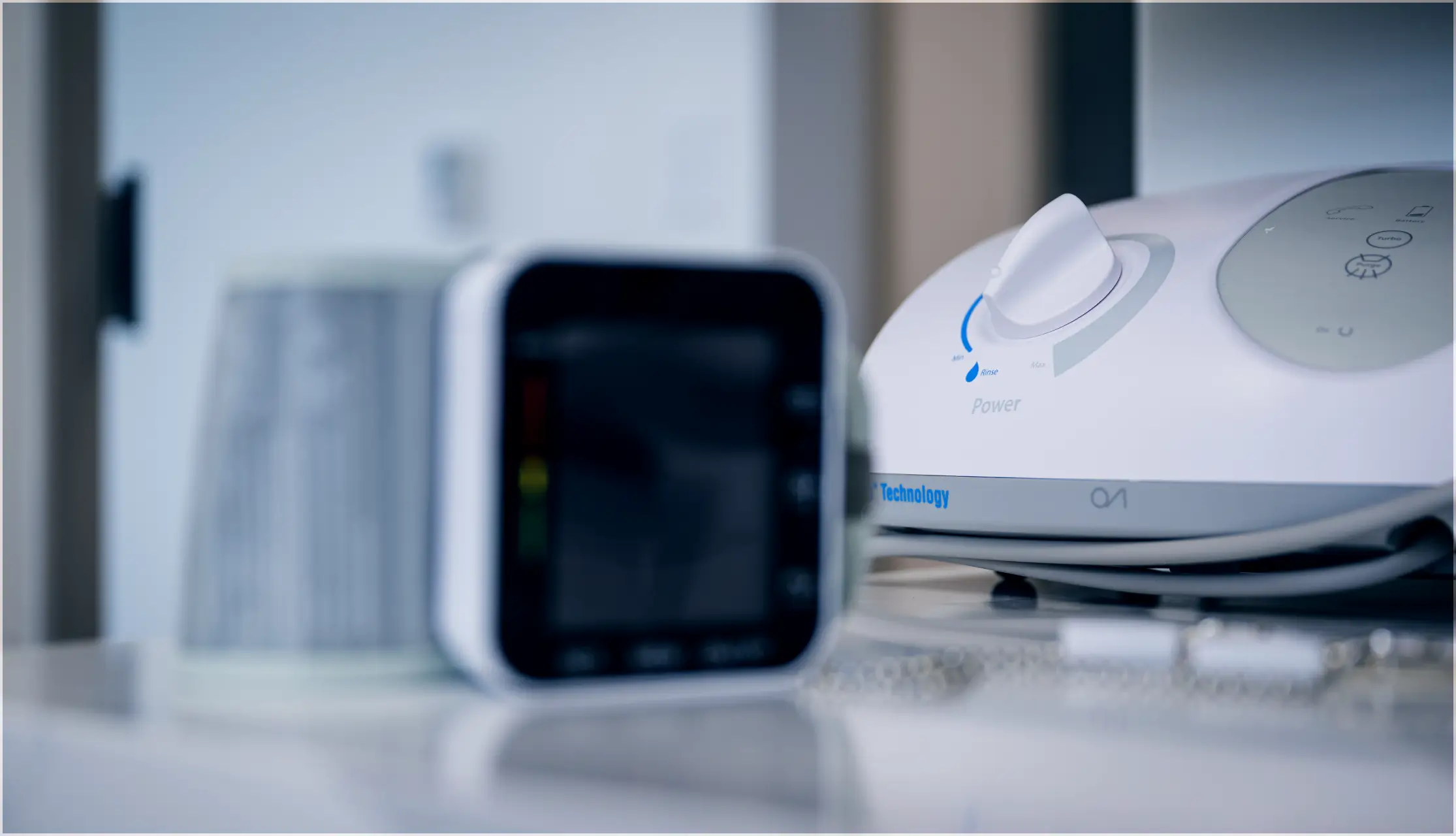 Close-up of a white electronic device with a control knob labeled 'Power' and a small screen device blurred in the foreground.