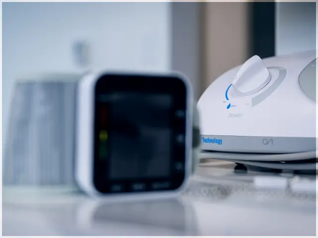Close-up of a white medical device with a dial labeled 'power' next to a blurred electronic monitor on a reflective surface.