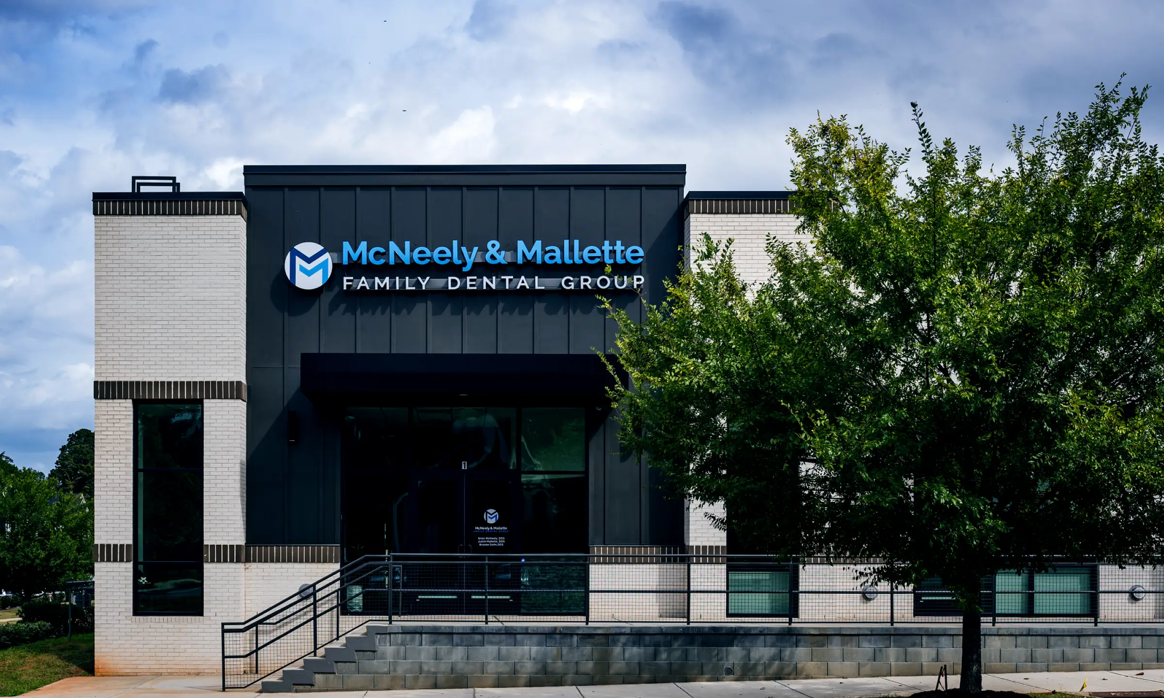 Front view of McNeely & Mallette Family Dental Group building with a green tree on the right and a cloudy sky.