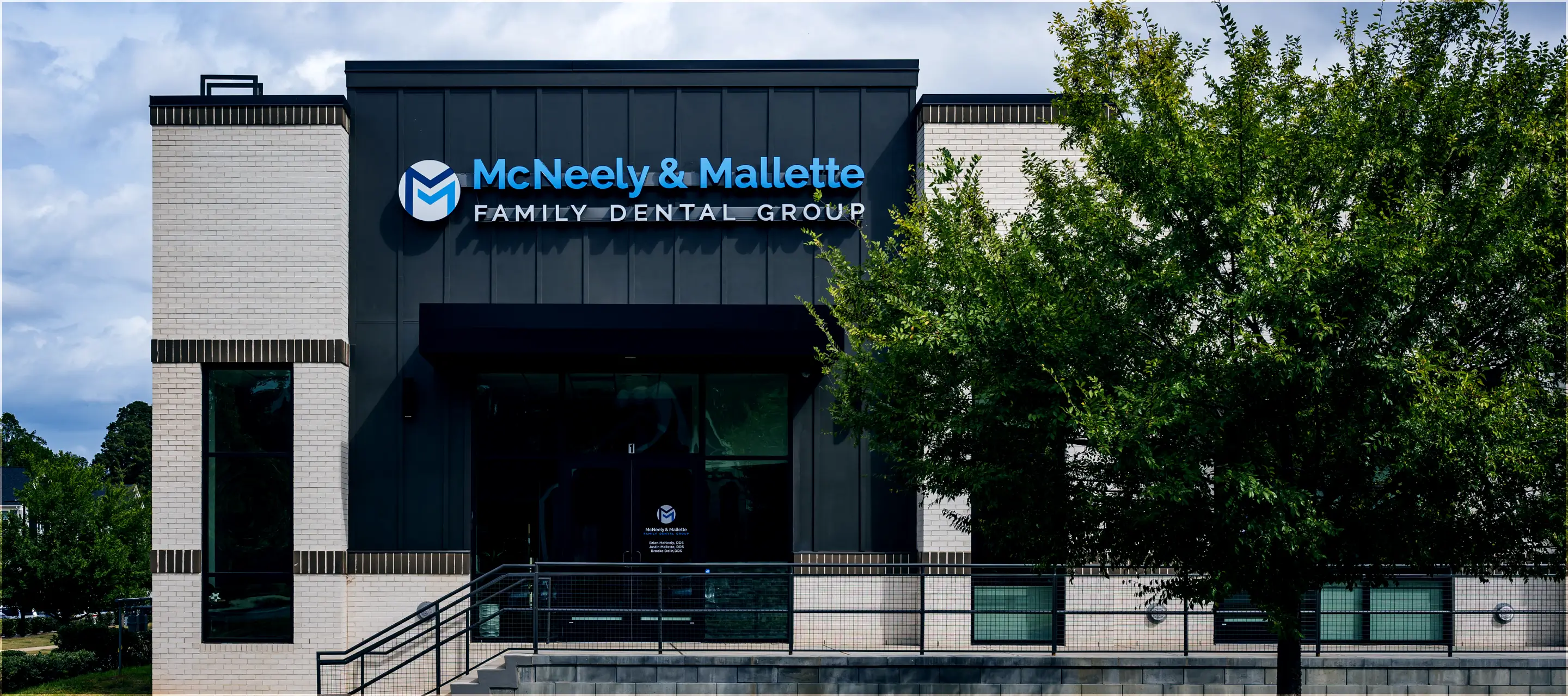 Front facade of McNeely & Mallette Family Dental Group building with black and white brick exterior and green trees in front.