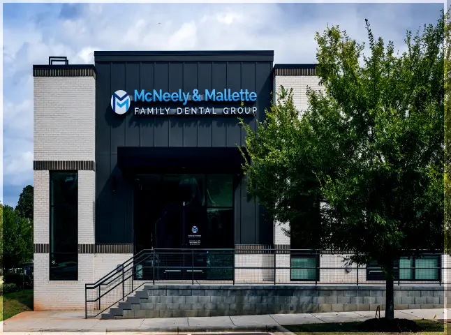 Modern building with white and dark gray exterior housing McNeely & Mallette Family Dental Group, with a tree on the right side.