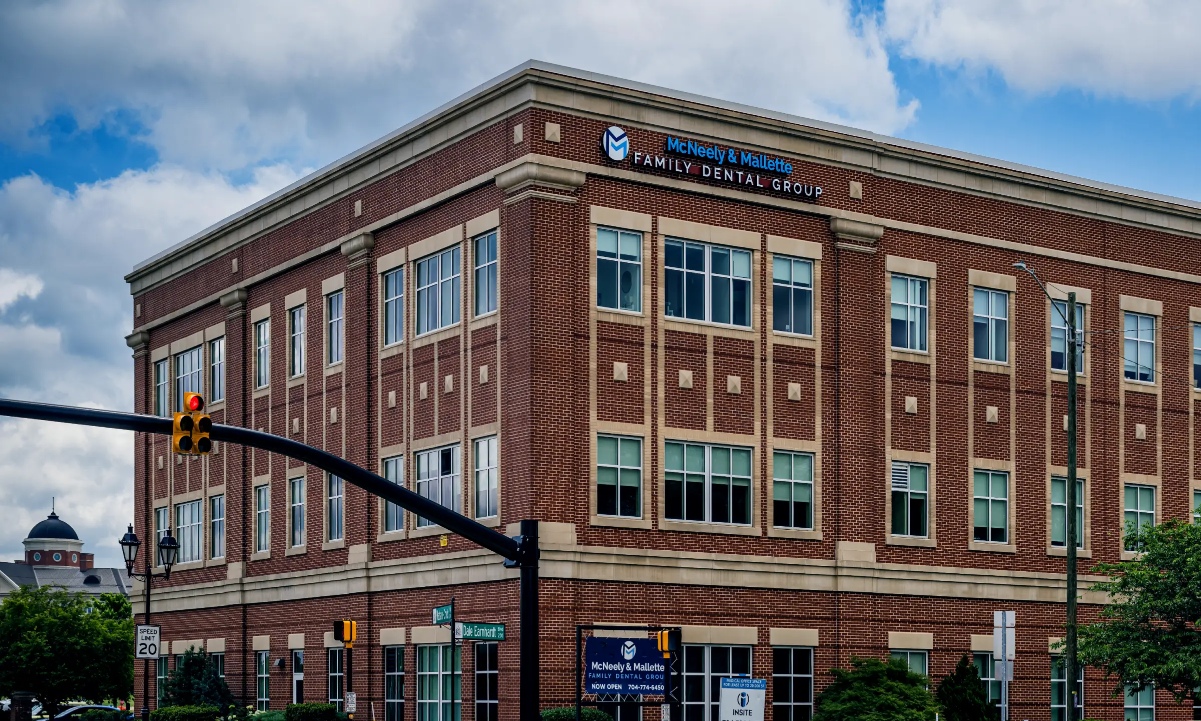 Brick office building housing McNeely & Mallette Family Dental Group at a street corner with a red traffic light and street signs.