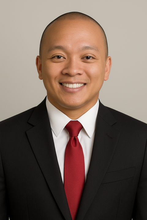 Smiling man wearing a black suit, white shirt, and red tie against a neutral background.