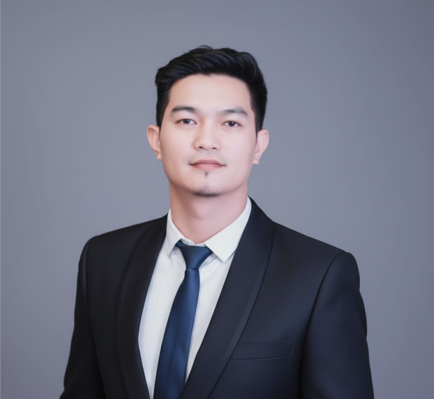 Professional portrait of a man in a dark suit, white shirt, and navy tie against a plain gray background.