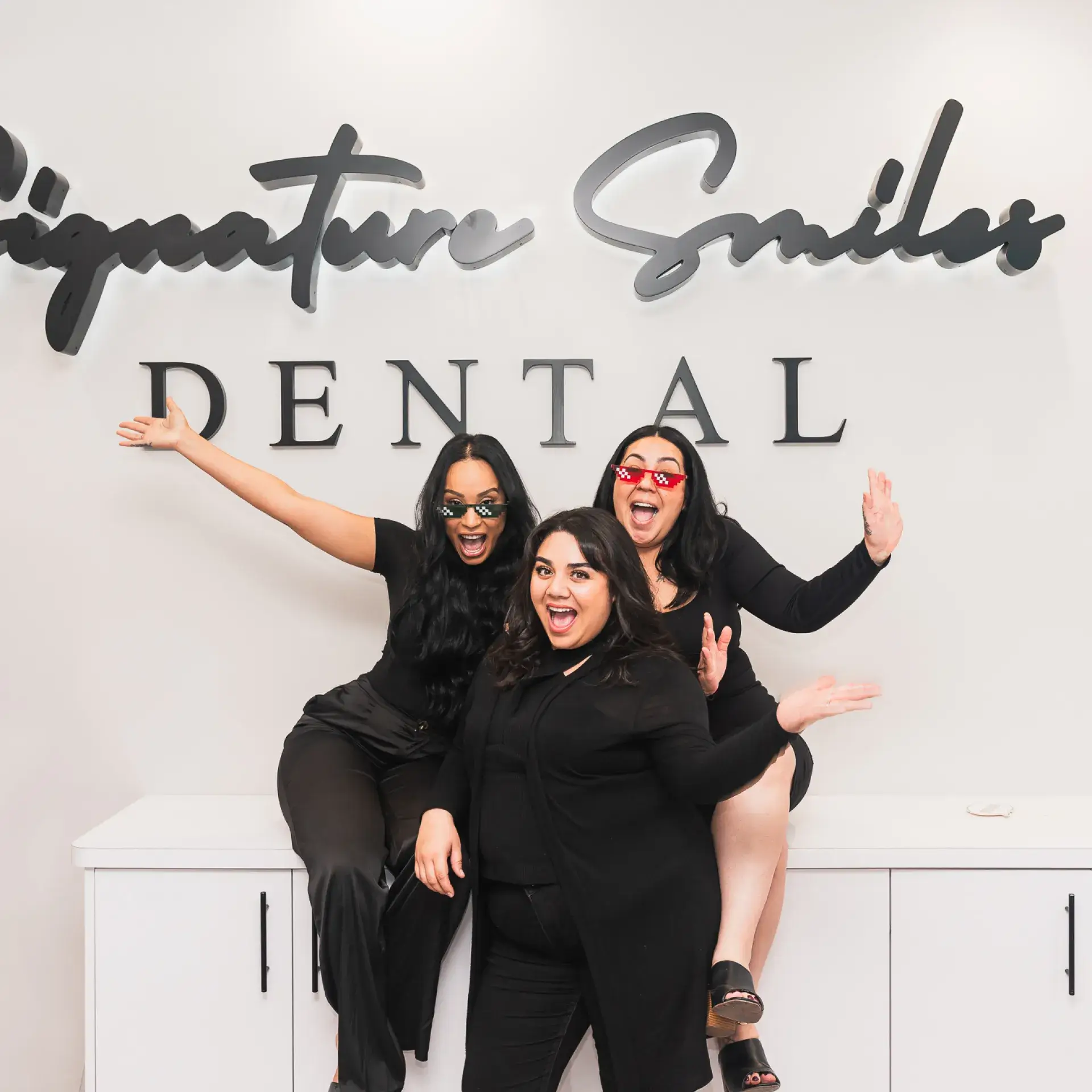 Three women posing for a picture in front of a dental sign.