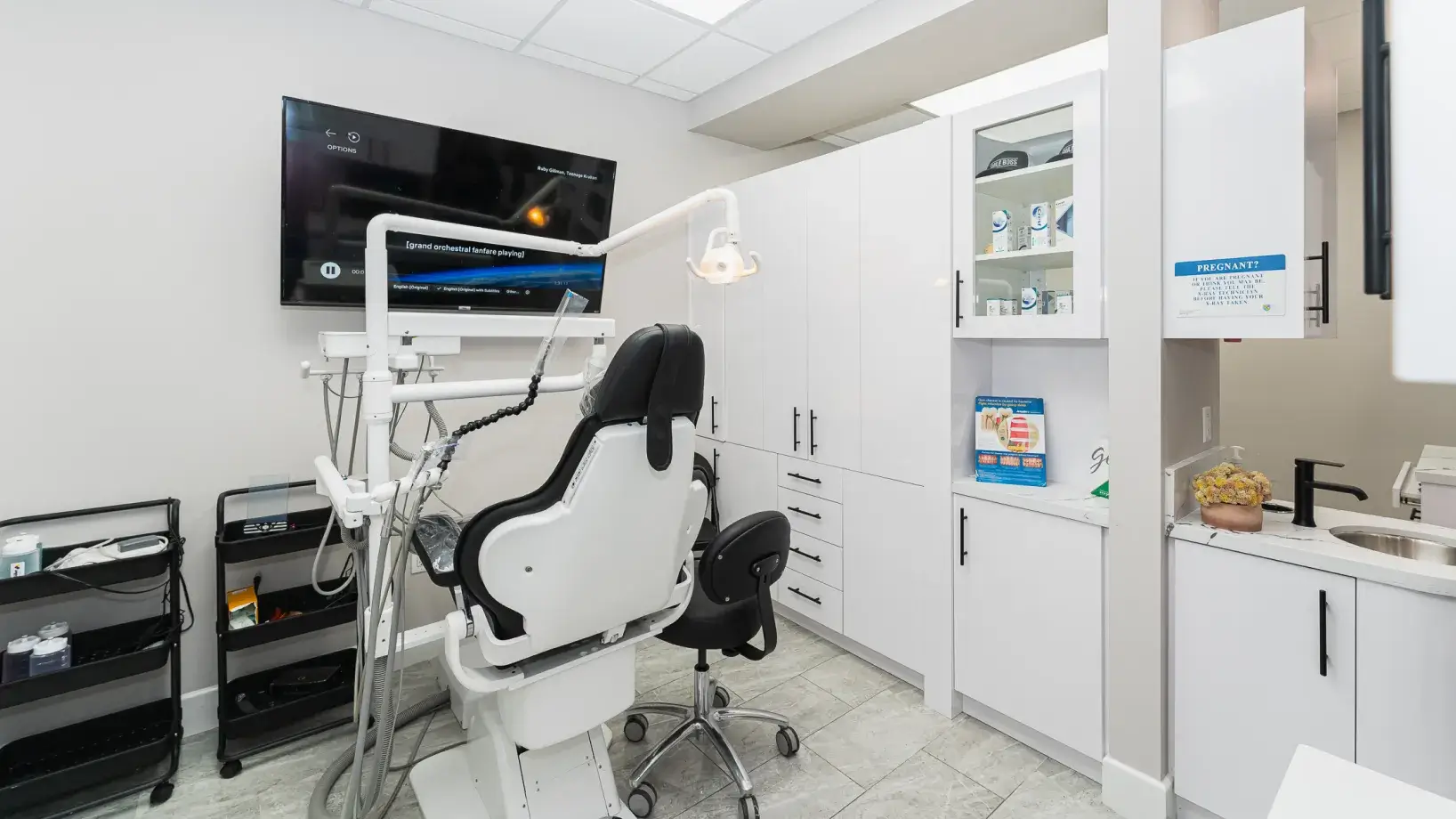 A dentist chair in a white room with a flat screen tv on the wall.