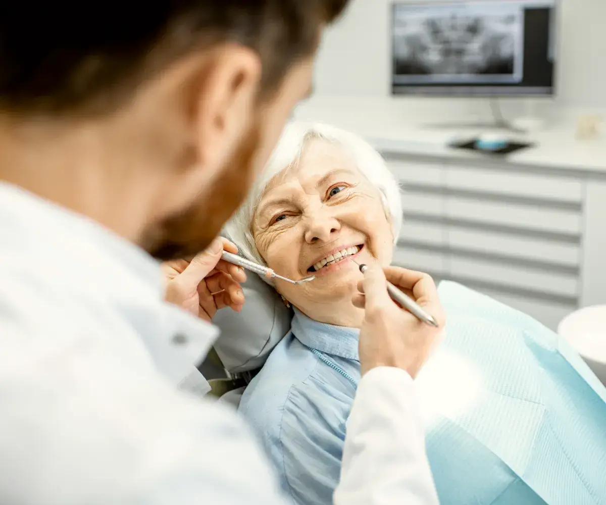 A woman sitting in a dentist chair with a toothbrush in her mouth.