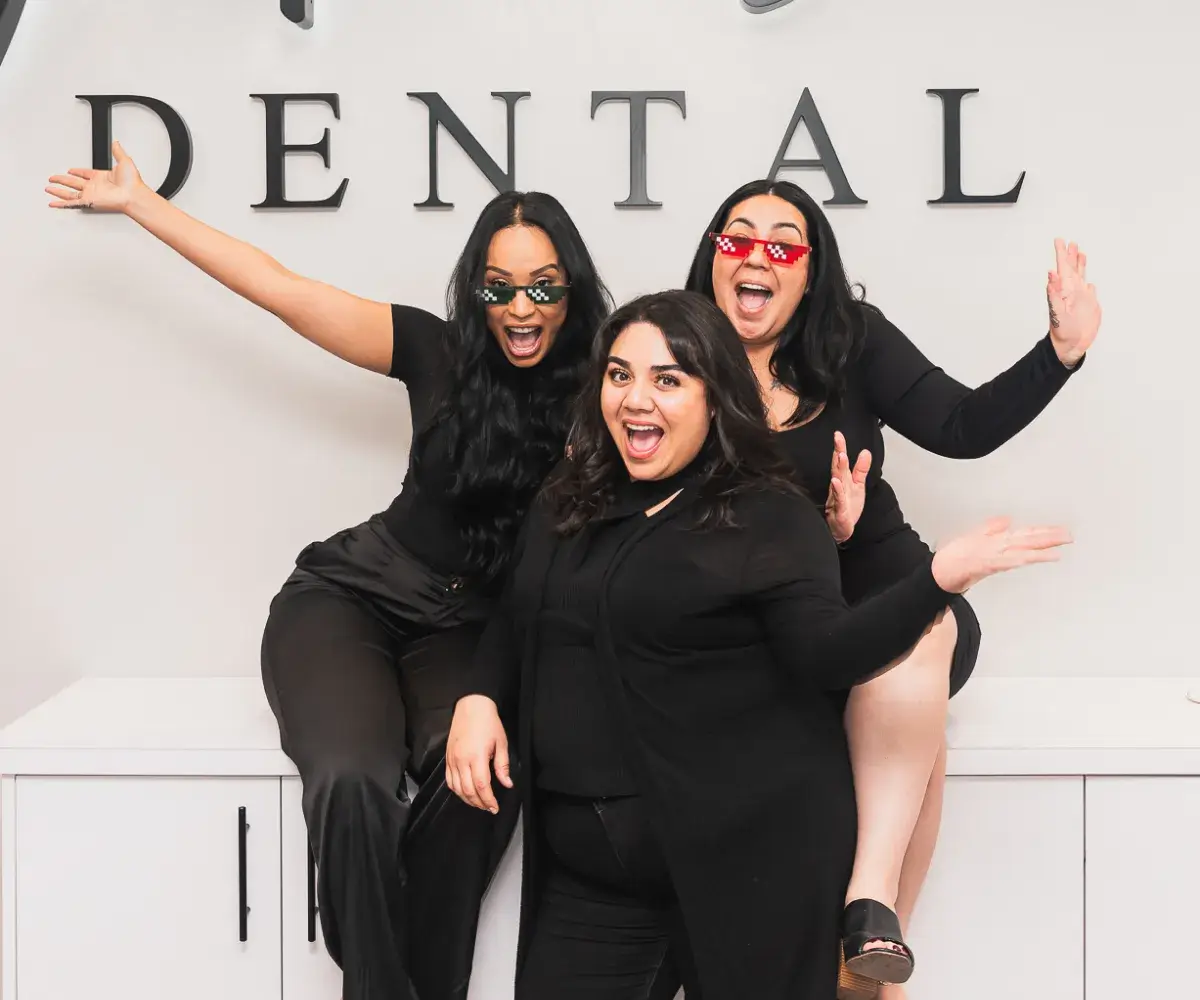 Three women posing for a photo in front of a dental sign.