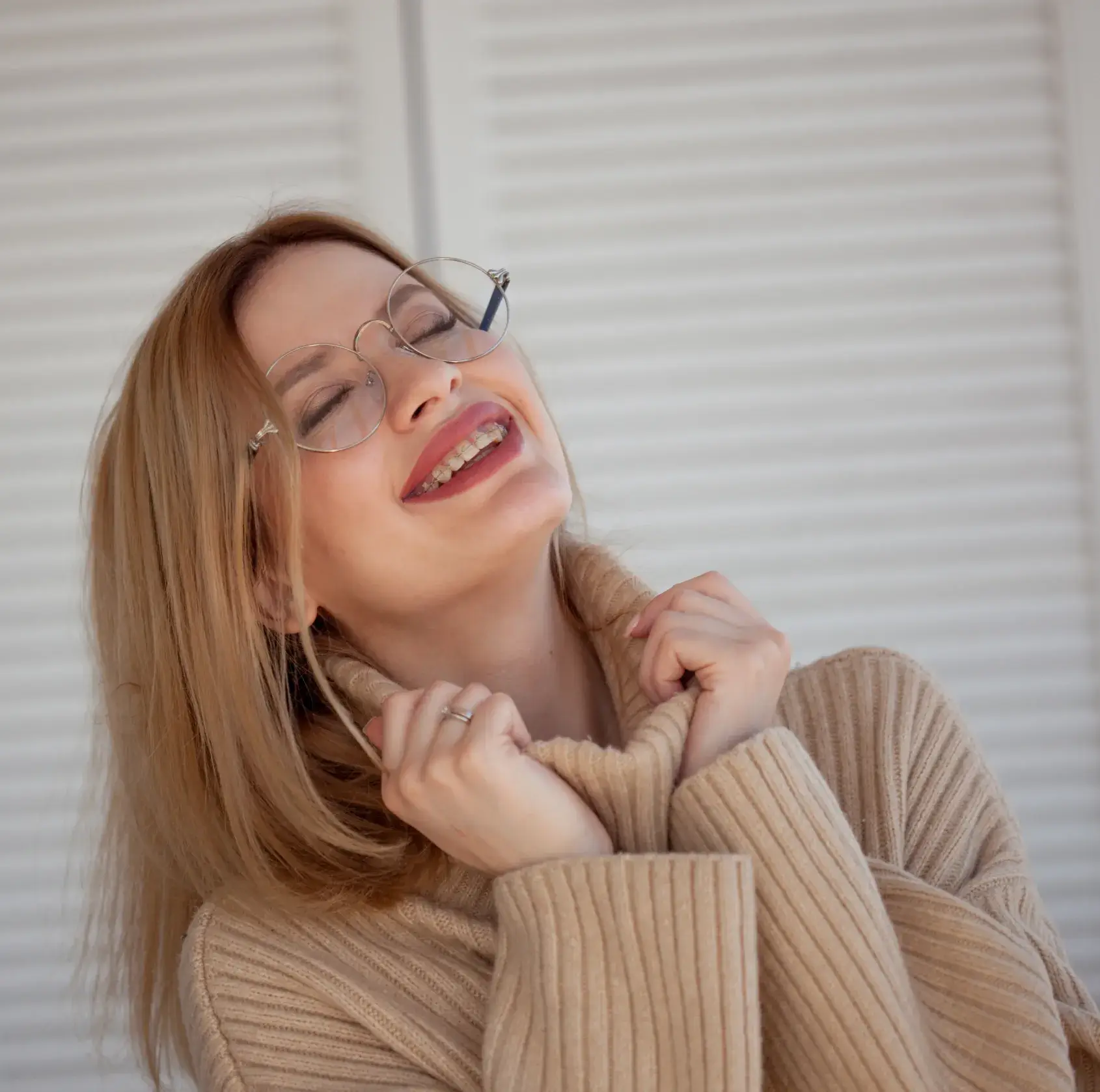 A woman wearing glasses and a sweater smiling.
