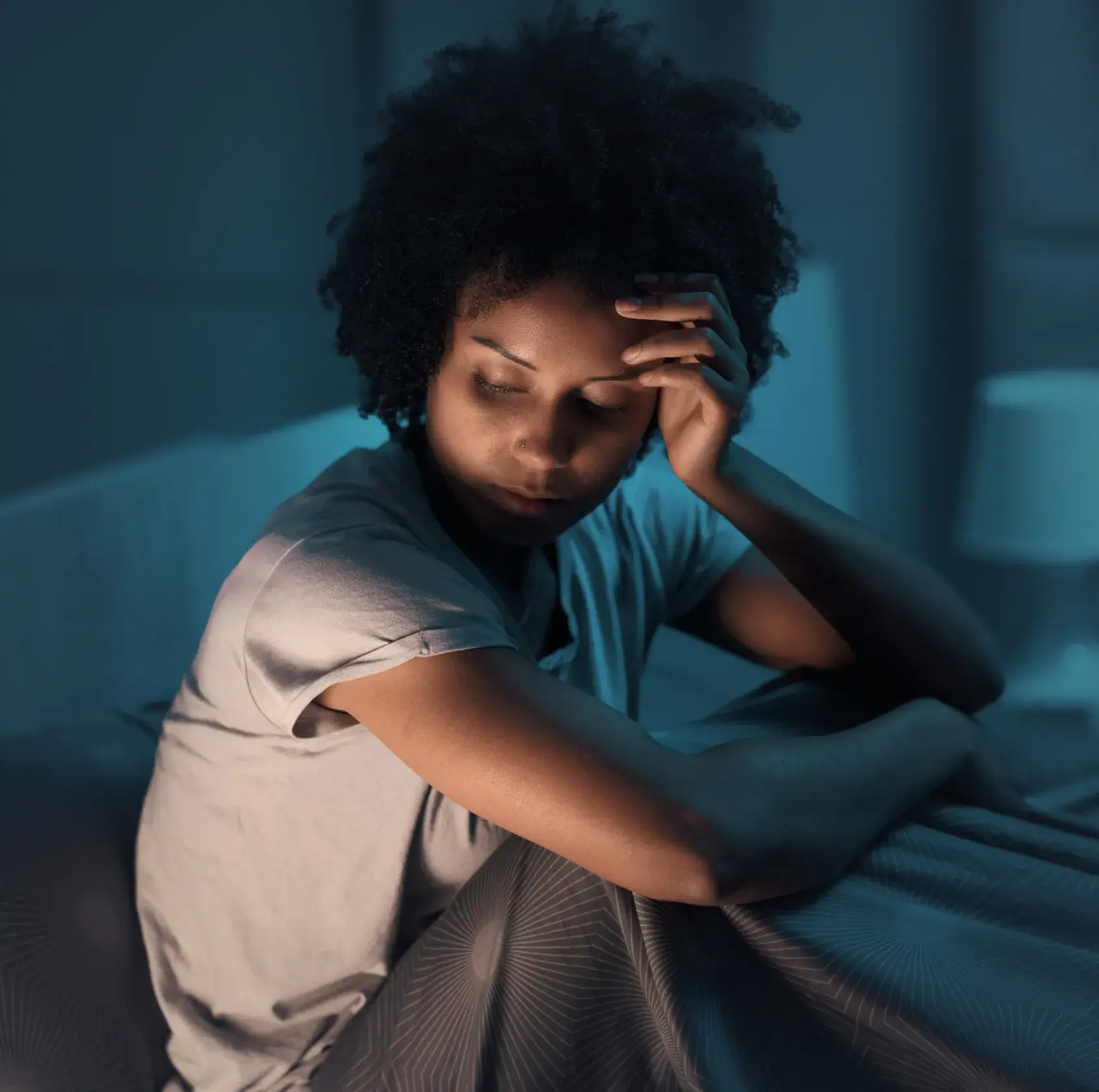 A woman sitting on a bed with her hand on her head.